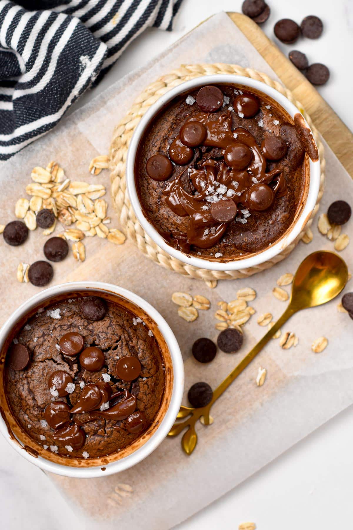 Chocolate Baked Oats served on two small ramekins, on a wooden board with a golden spoon.