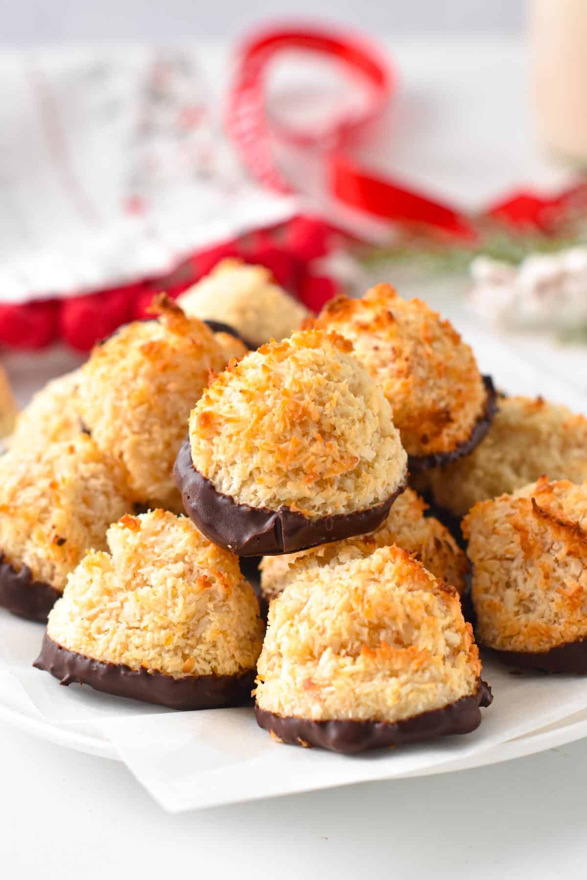 A plate filled with a stack of vegan coconut macaroons with toasted coconut and chocolate dipped.