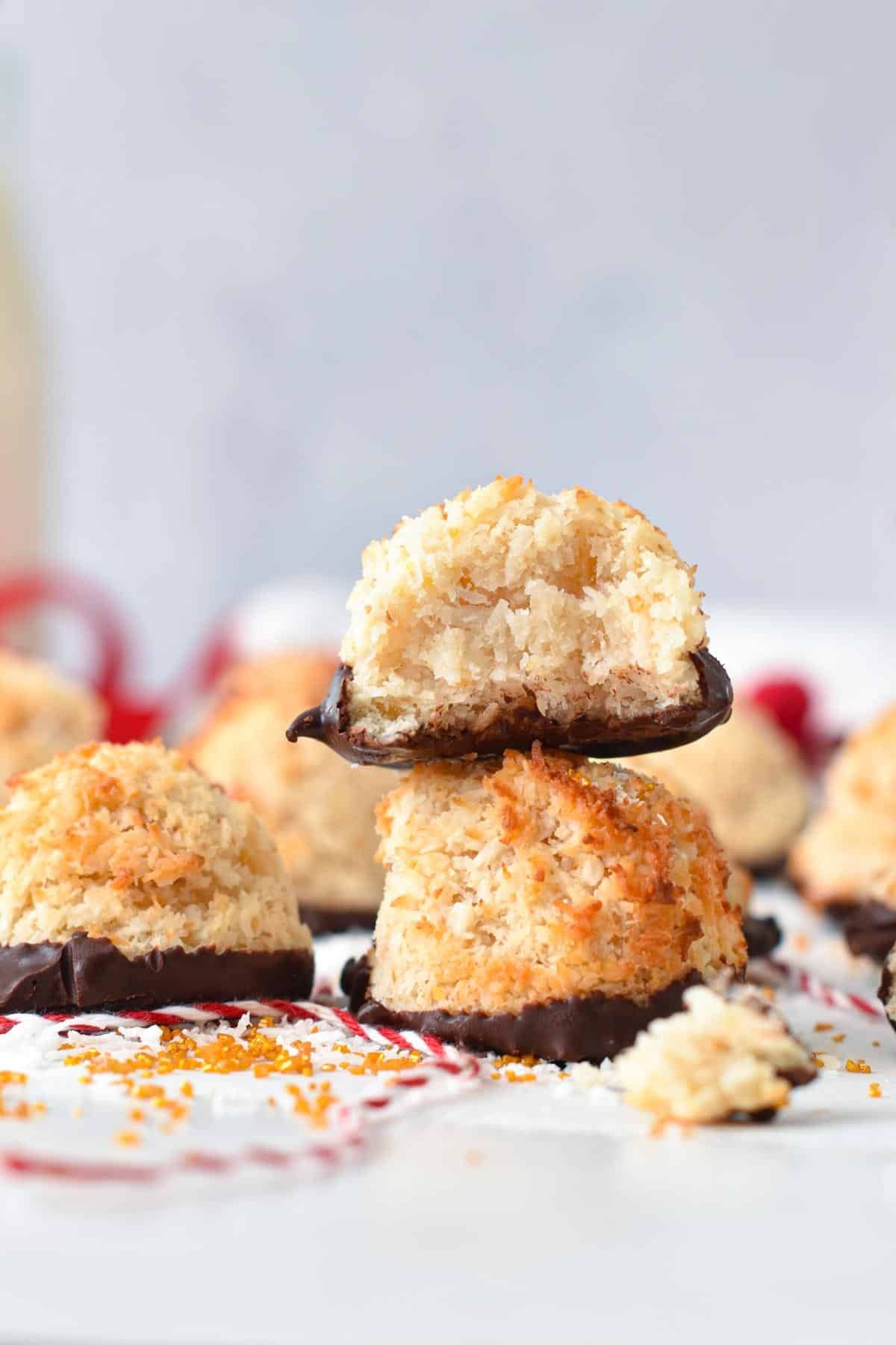 Two vegan coconut macaroons with a dipped chocolate bottom, stacked with the top on half bitten.