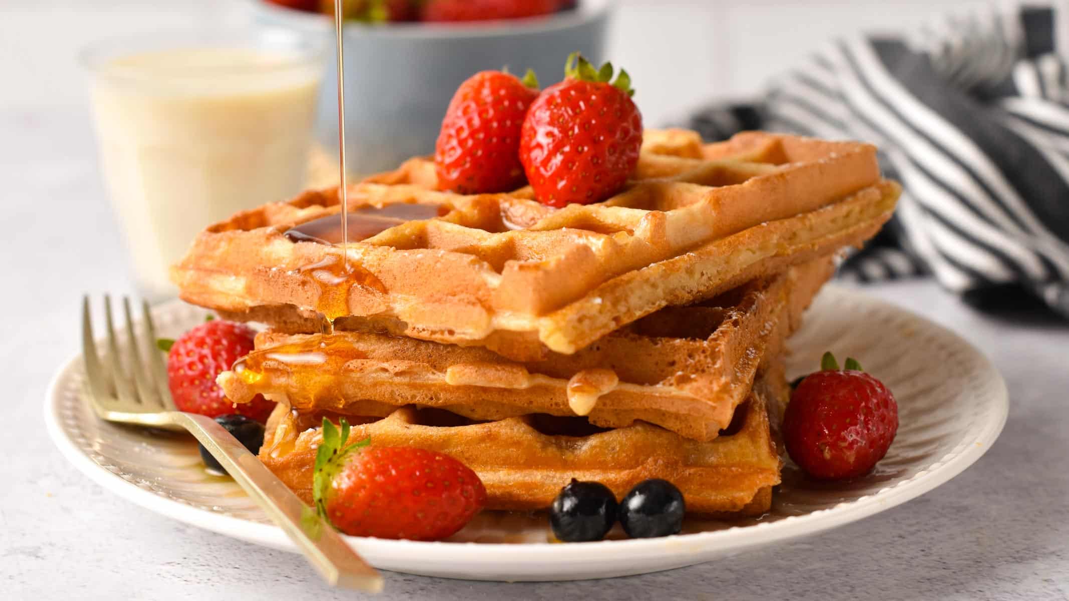 Vegan Protein Waffles stacked on a plate and decorated with strawberries and blueberries.