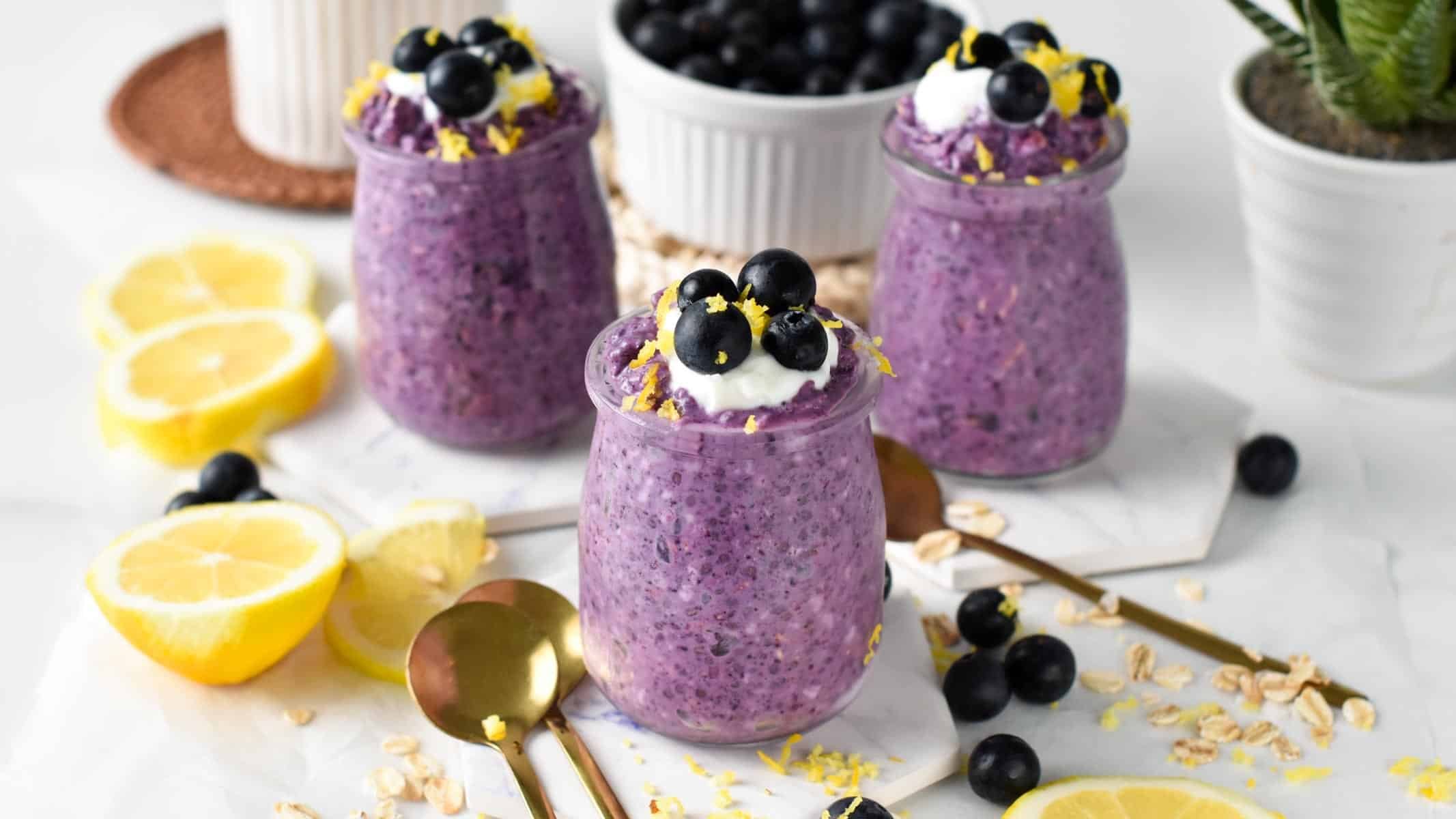 Three jars of blueberry overnight oats on a table full of lemon slices and blueberries.