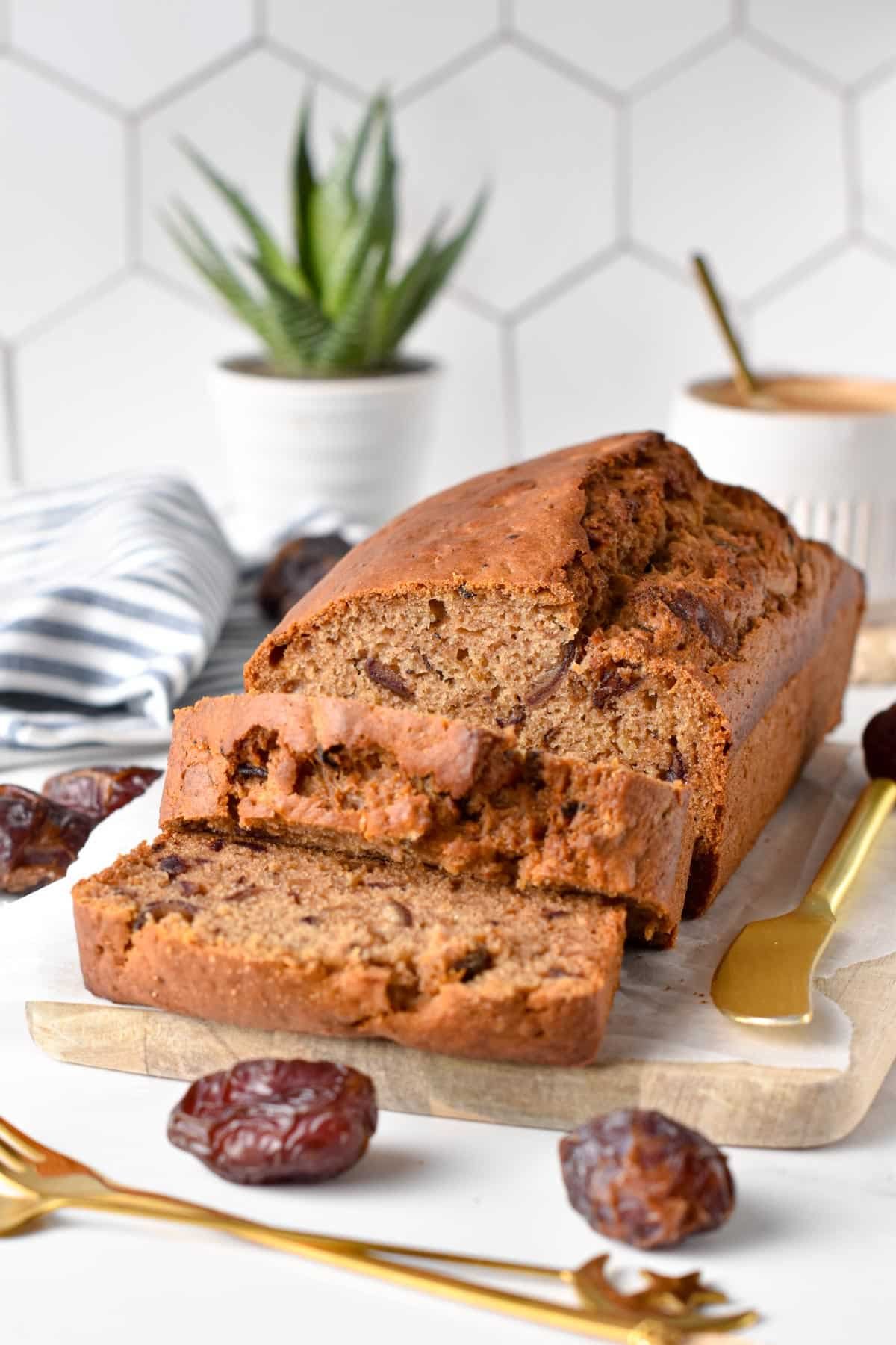 Date loaf on a chopping board with dates and golden cutlery around it.