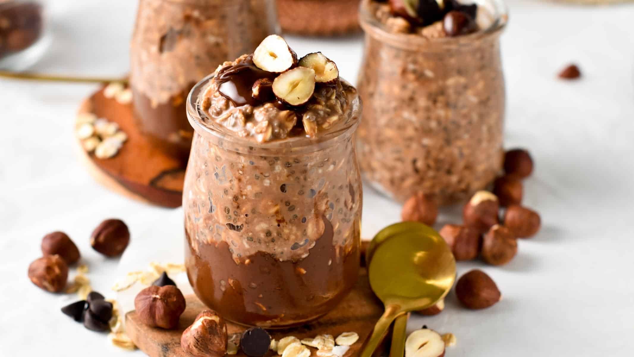 Nutella Overnight Oats jars with fresh hazelnuts and golden spoons.