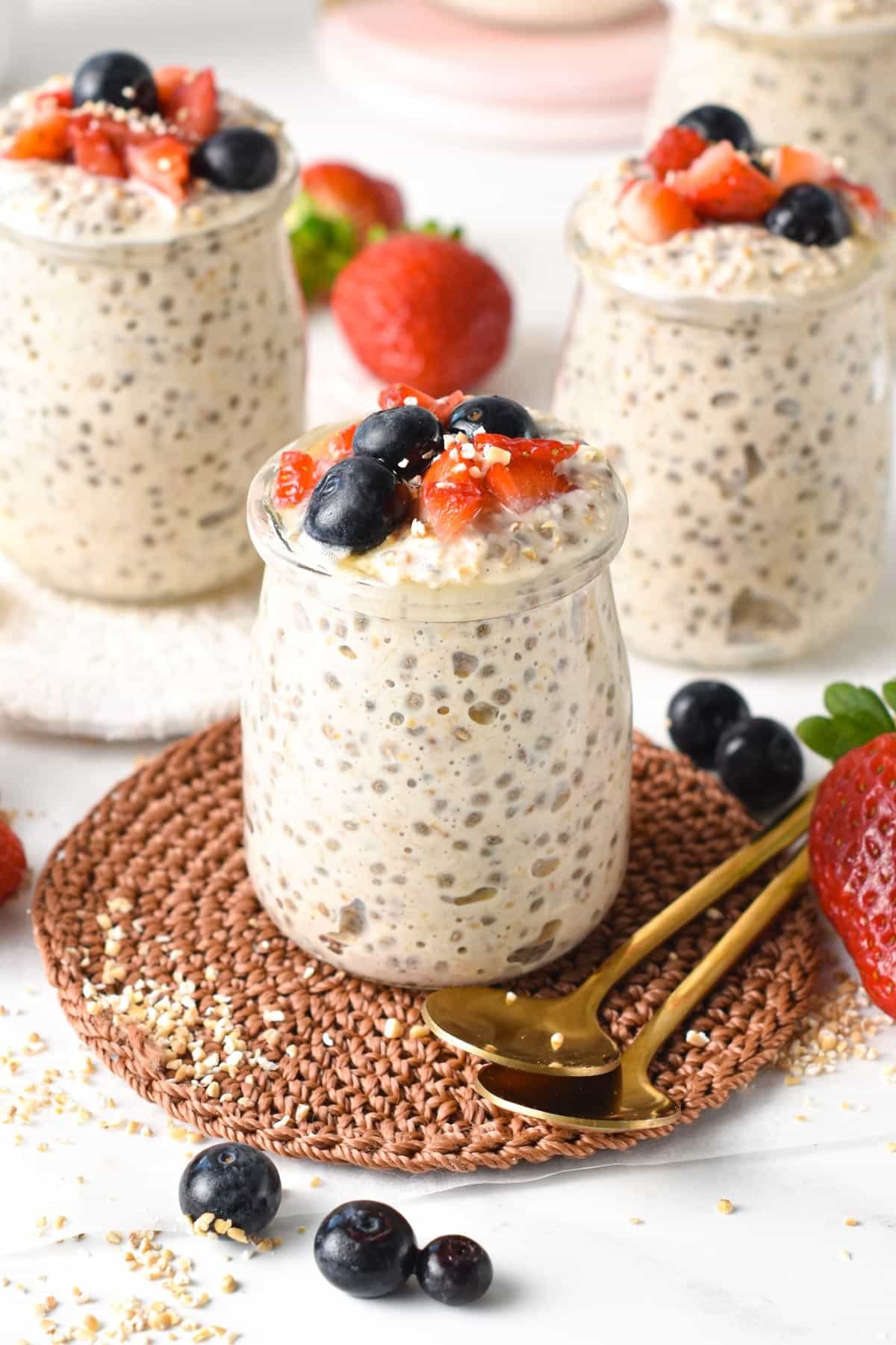 Four jars of Overnight Steel Cut Oats on coasters surrounded by fresh strawberries and blueberries.