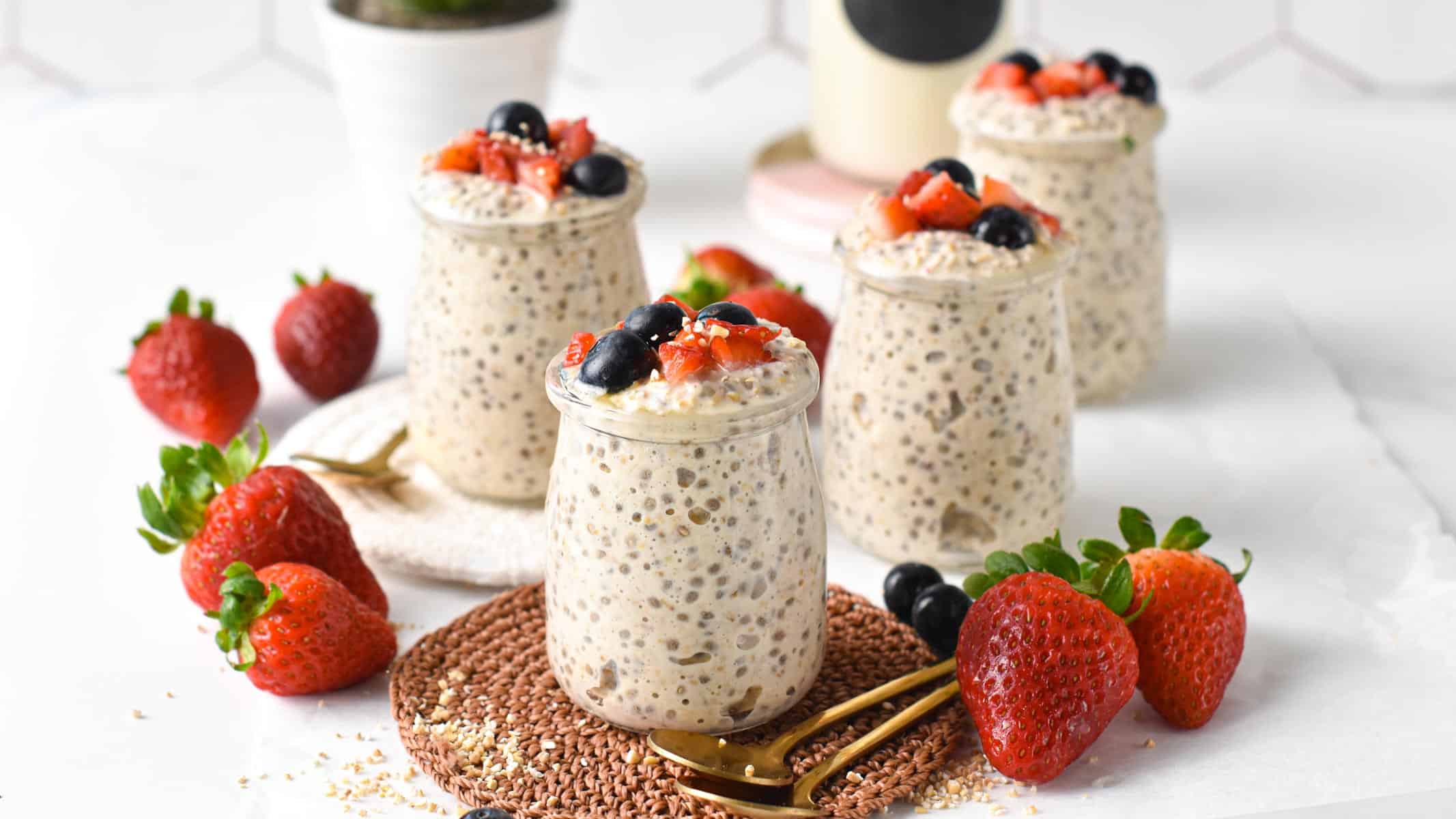 Overnight Steel Cut Oats in jars on a white table with fresh strawberries.