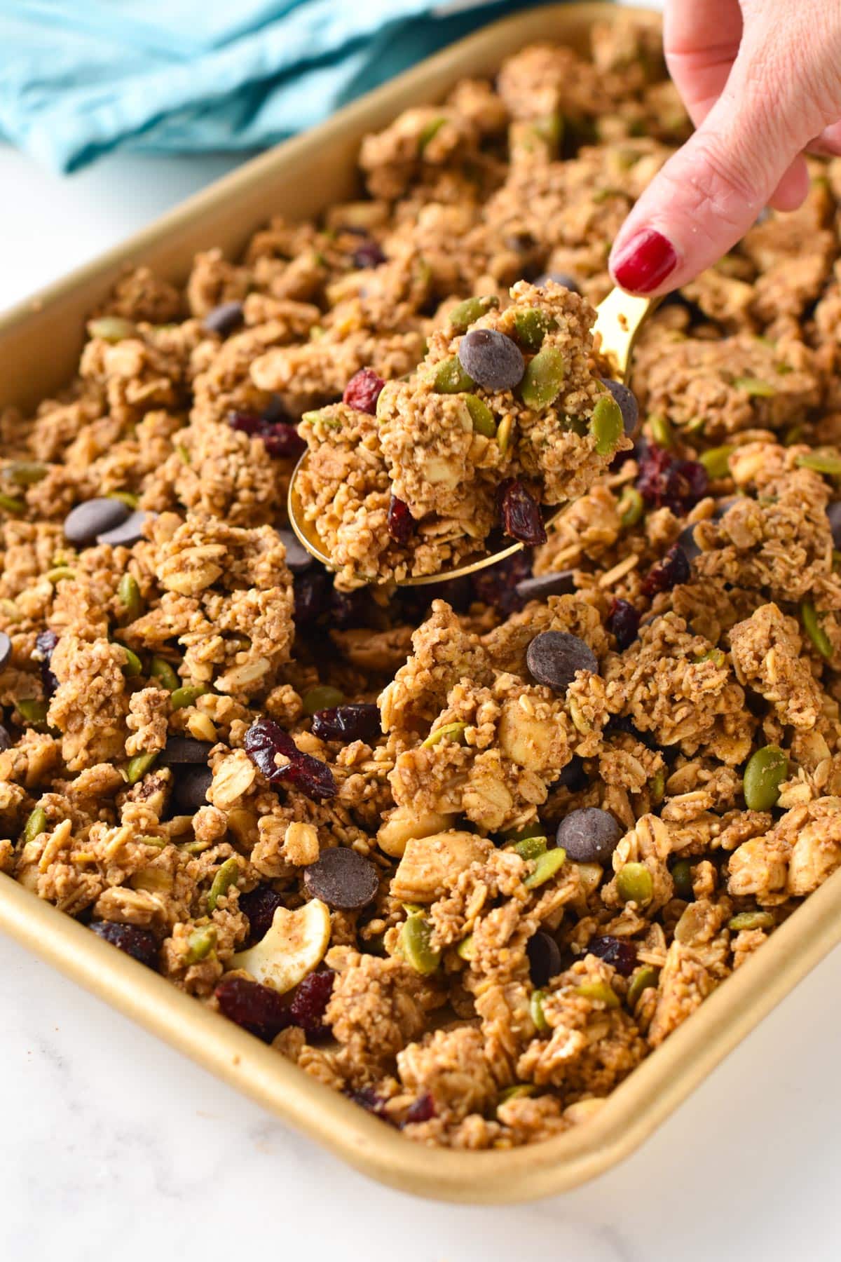 A golden spoon taking a portions of Steel Cut Oats Granola off the baking sheet.