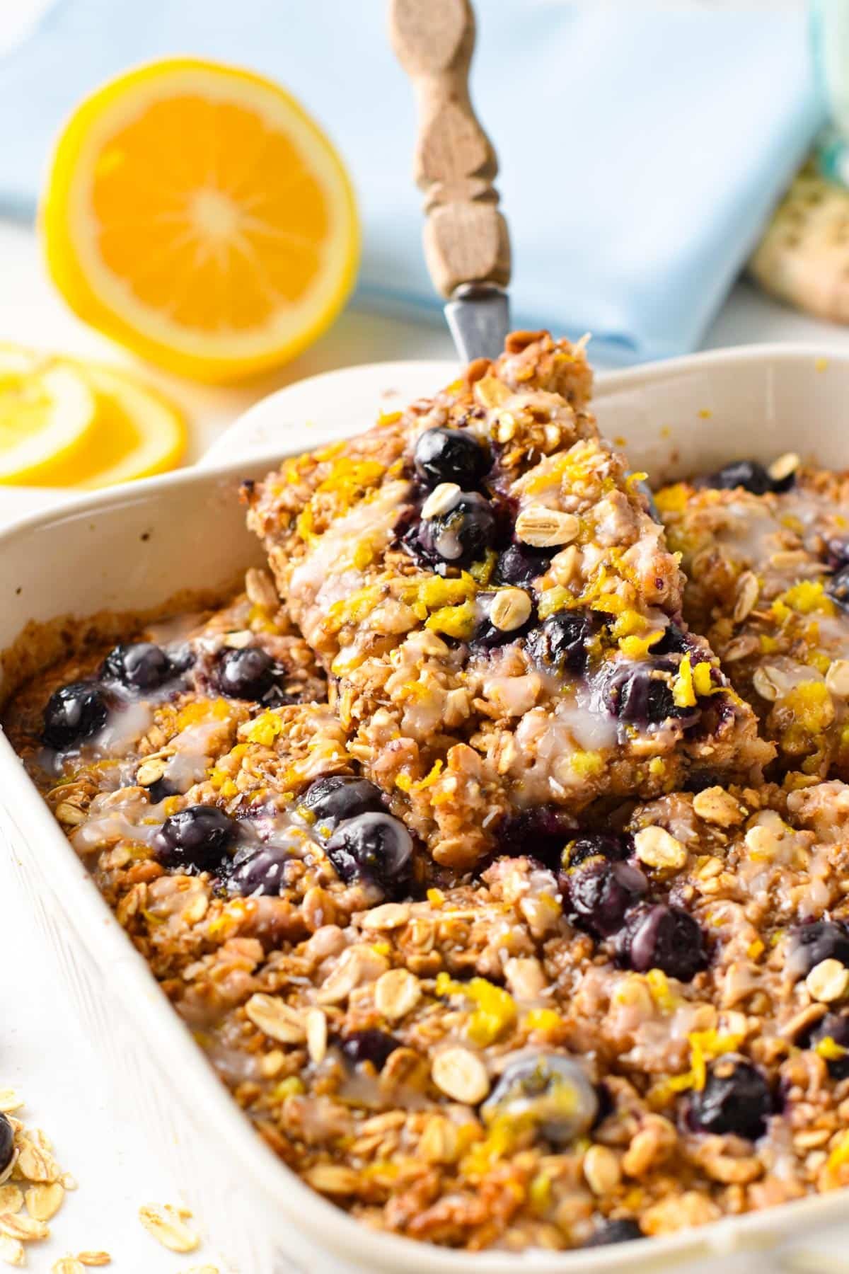 Lemon blueberry baked oatmeal in a large ceramic pan with a slice on a spatula.