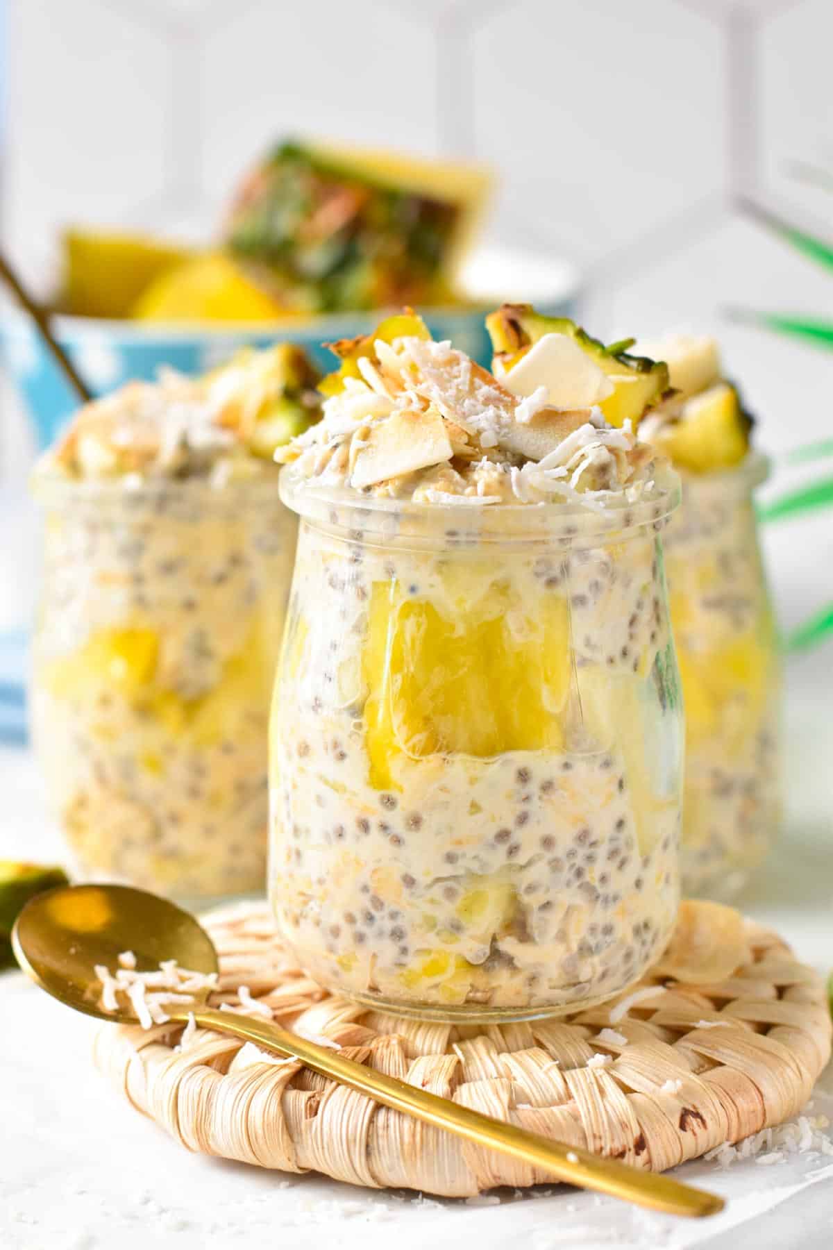 Pina Colada Overnight Oats in three jars decorated with coconut flakes and pineapple chunks.