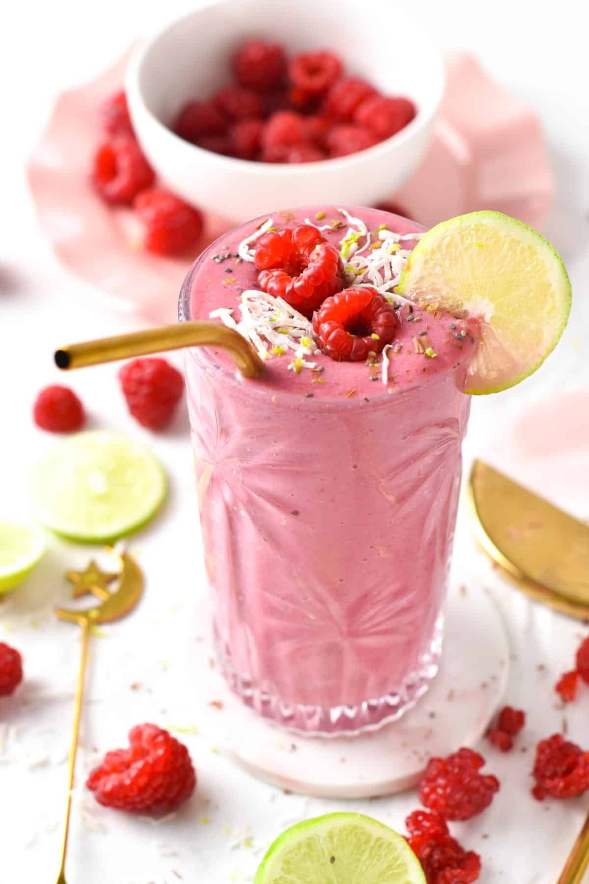 Raspberry Smoothie decorated with a slice of lime, fresh raspberries, and shredded coconut.