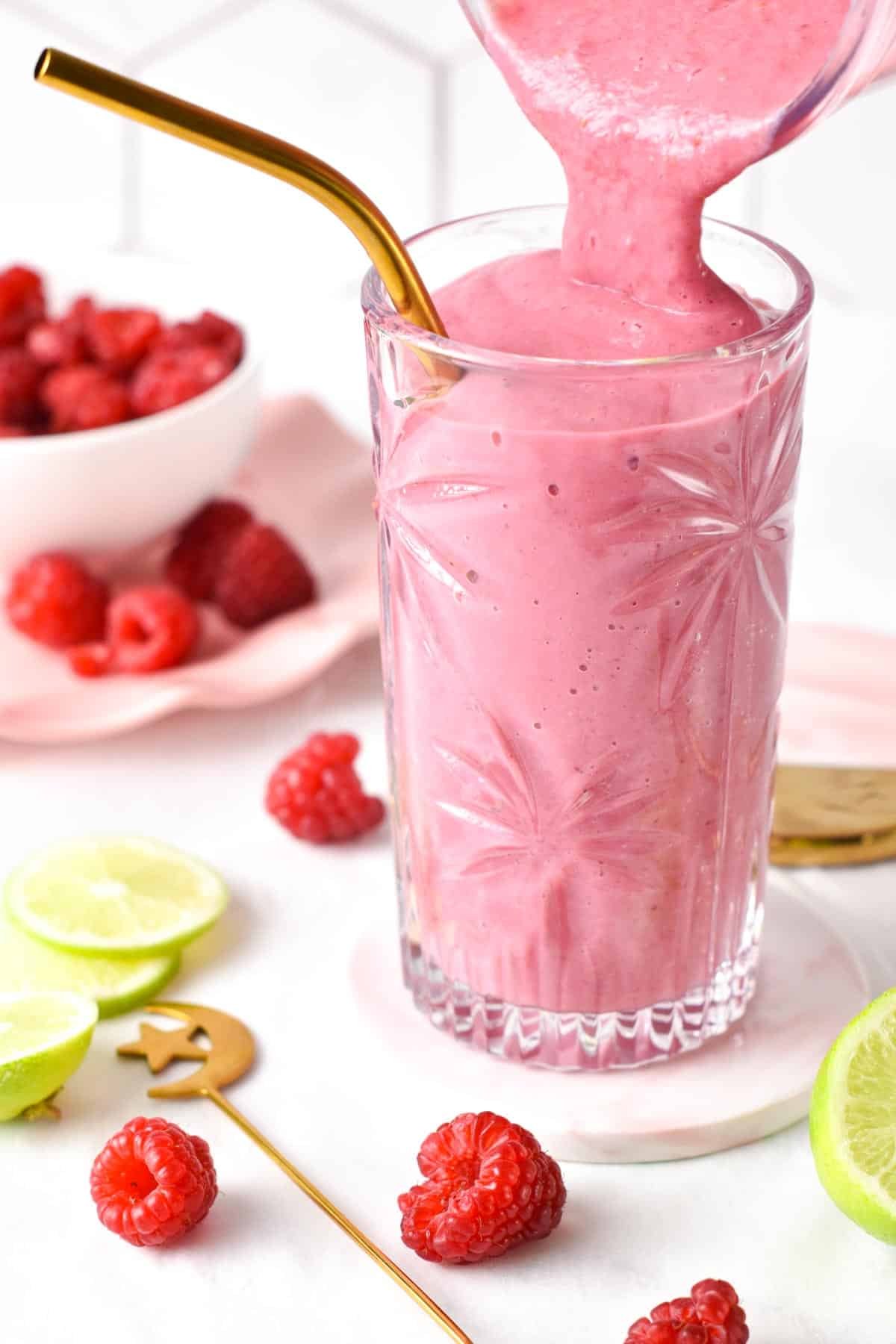 Pouring Raspberry Smoothie in a tall glass with a golden straw.