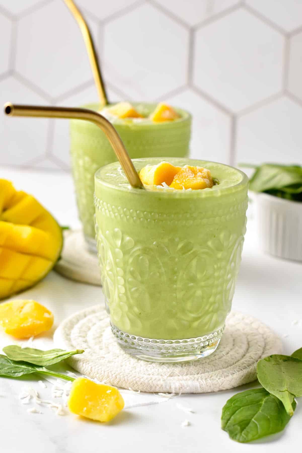 Mango Spinach Smoothie in two small glass on natural coasters.