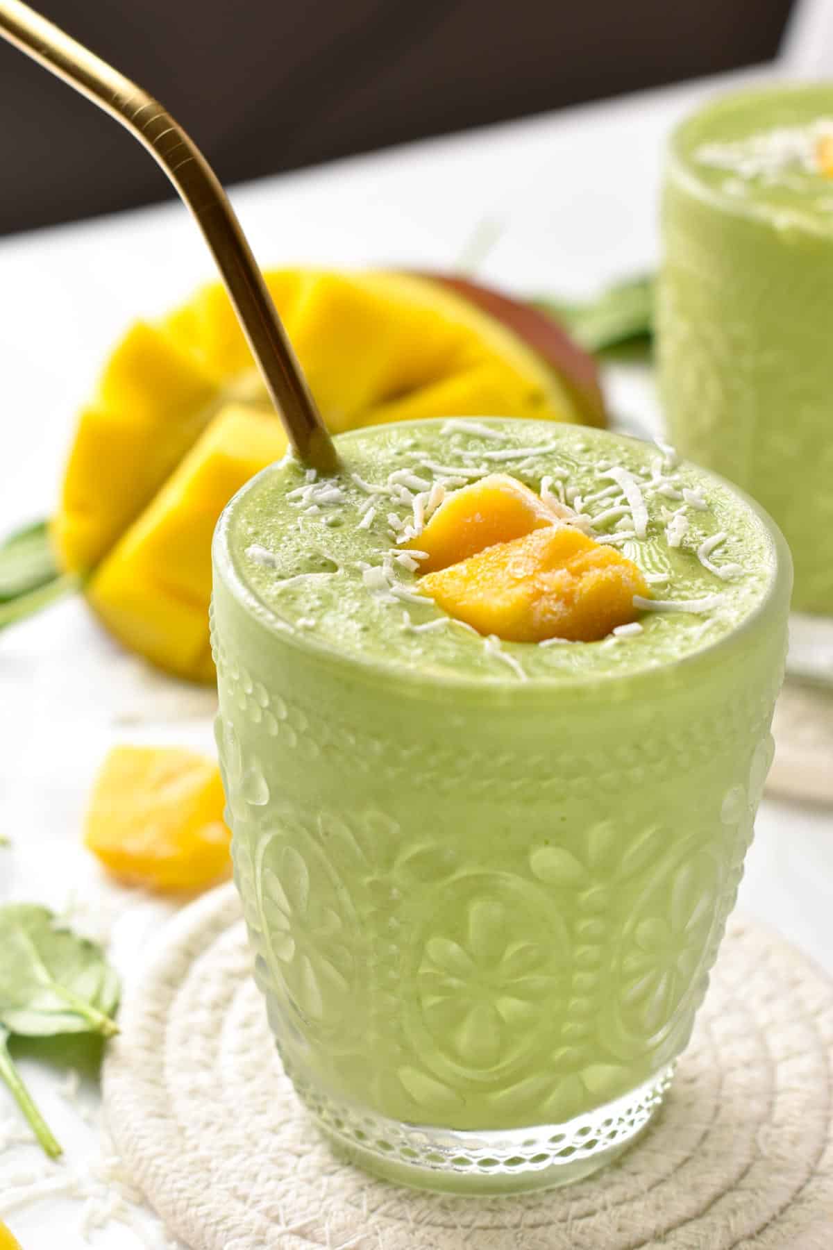 Mango Spinach Smoothie in a small glass decorated with fresh mango and shredded coconut.