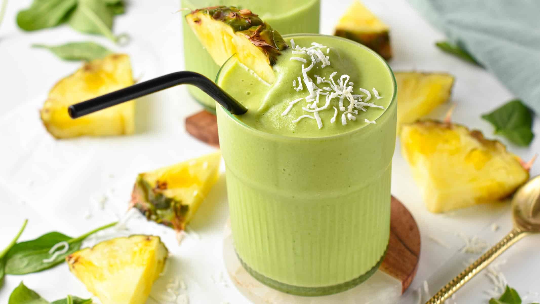 Spinach pineapple smoothie in a small glass with fresh pineapple and a black straw.