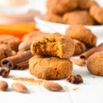 a stack of almond flour pumpkin cookies with one bitten cookie on top of the stack showing the moist pumpkin texture of the cookies