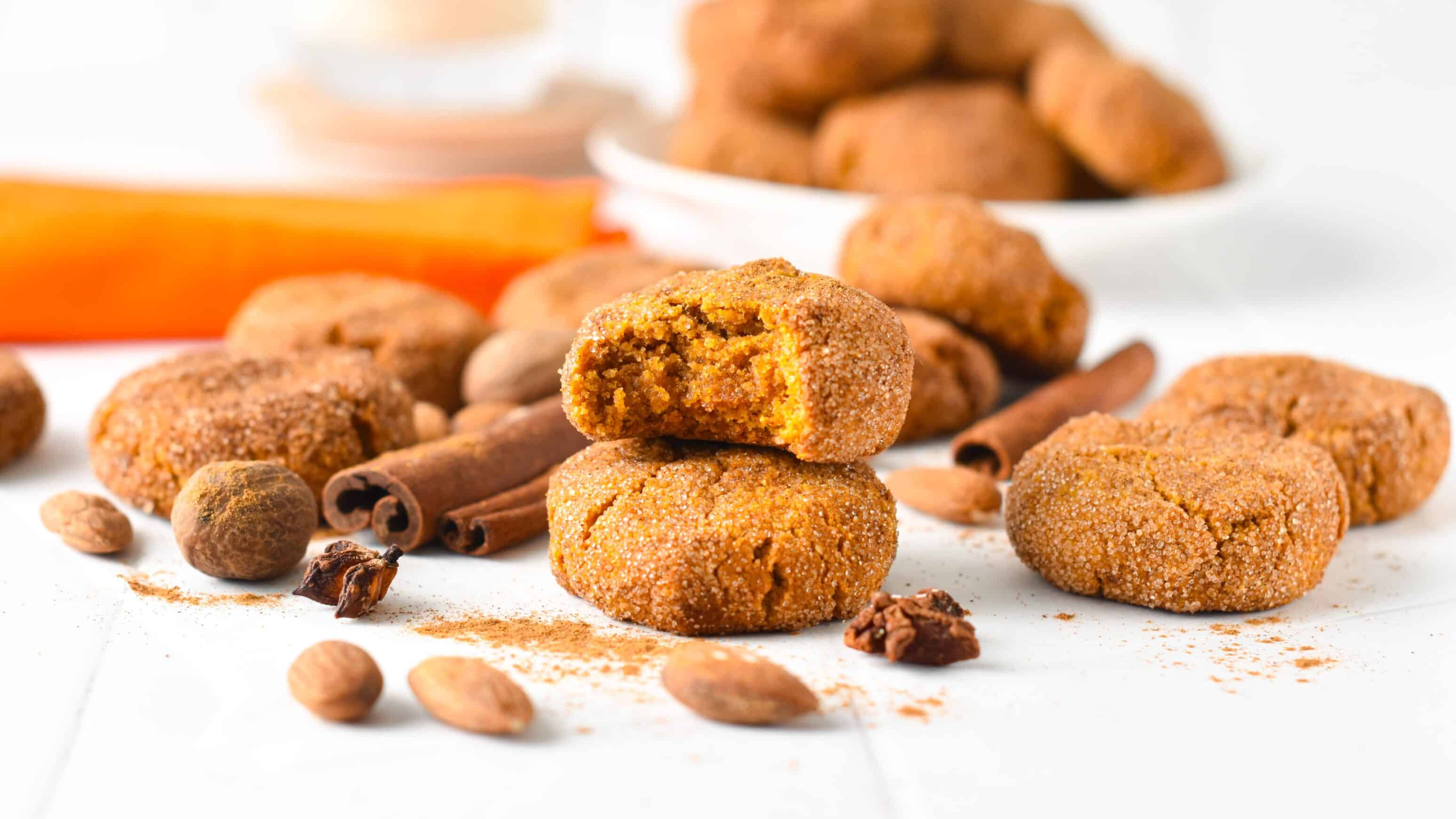 a stack of almond flour pumpkin cookies with one bitten cookie on top of the stack showing the moist pumpkin texture of the cookies