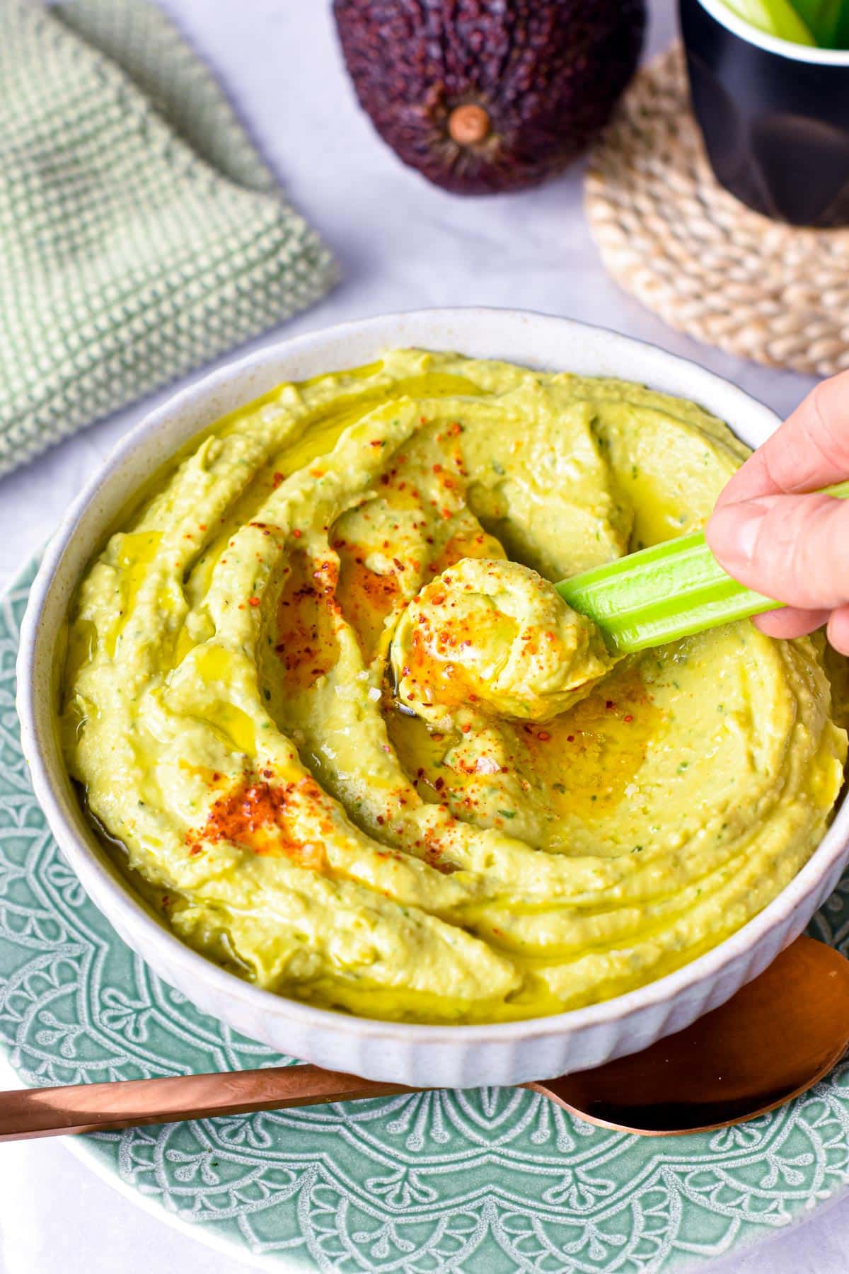 Avocado Hummus with a stick of celery dipped into it.