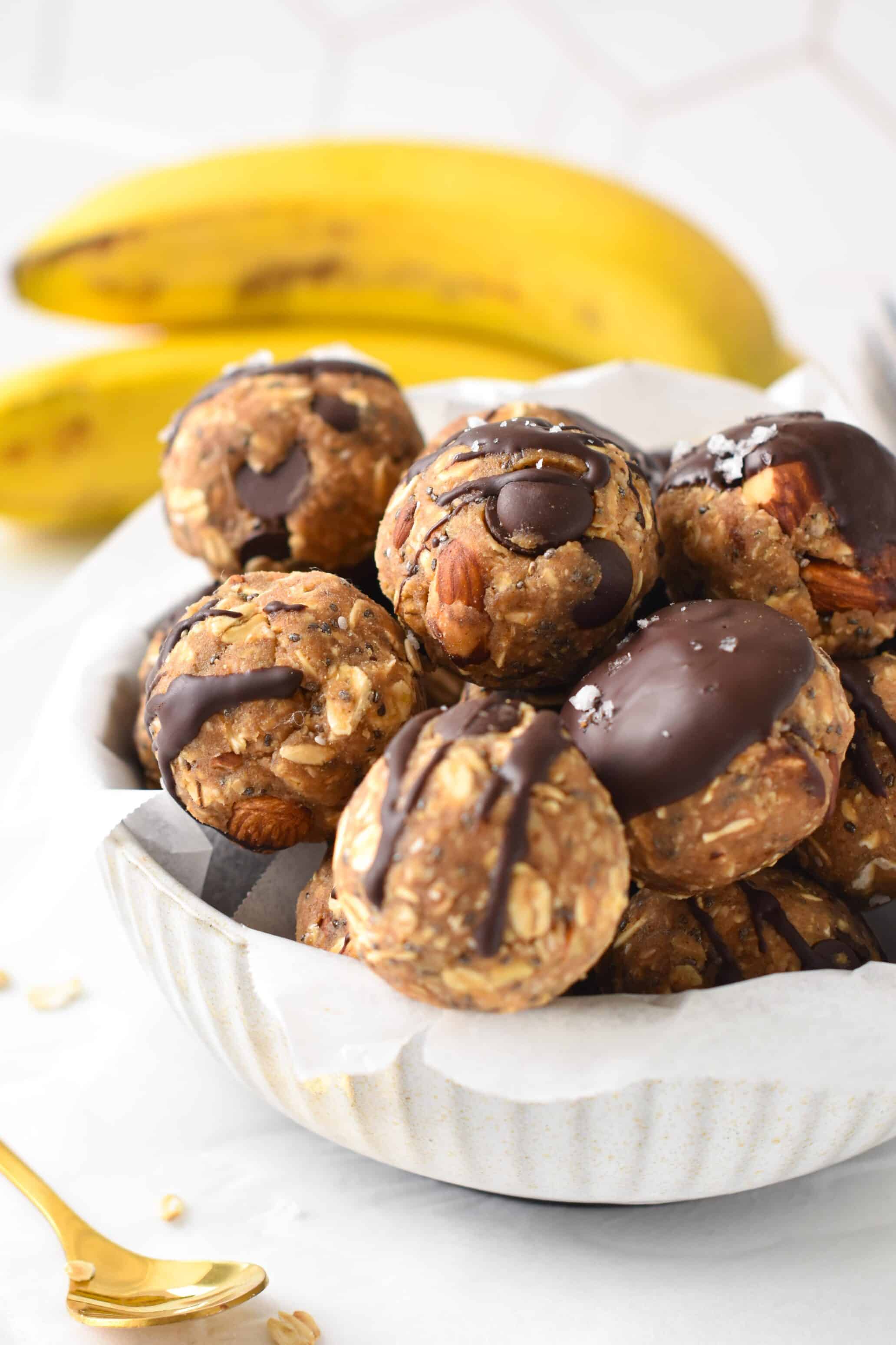 Banana Protein Balls in a large white bowl, decorated with melted chocolate and salt flakes.