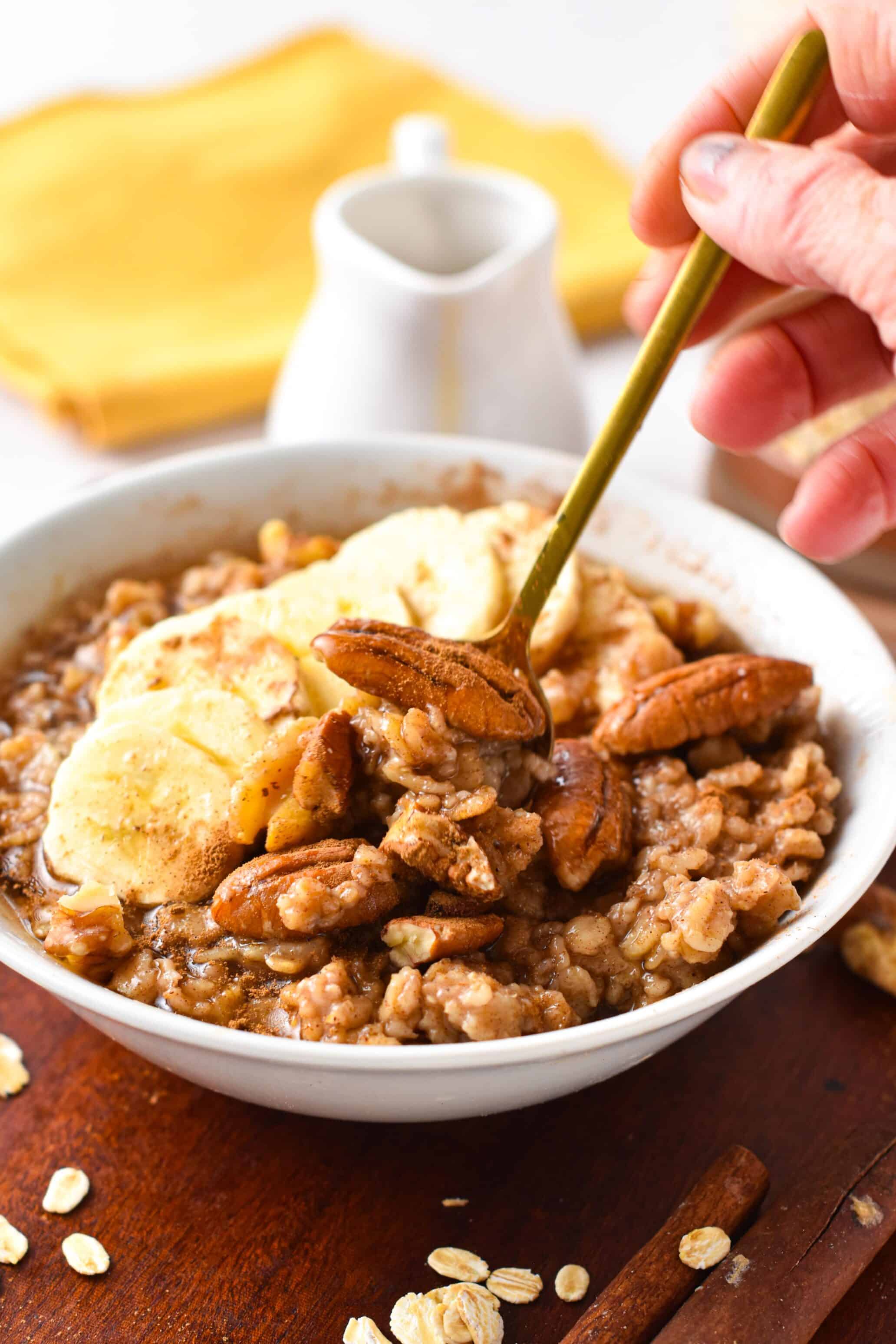 A bowl oaf cinnamon oatmeal with a golden spoon, served with banana slices, pecans and walnuts.