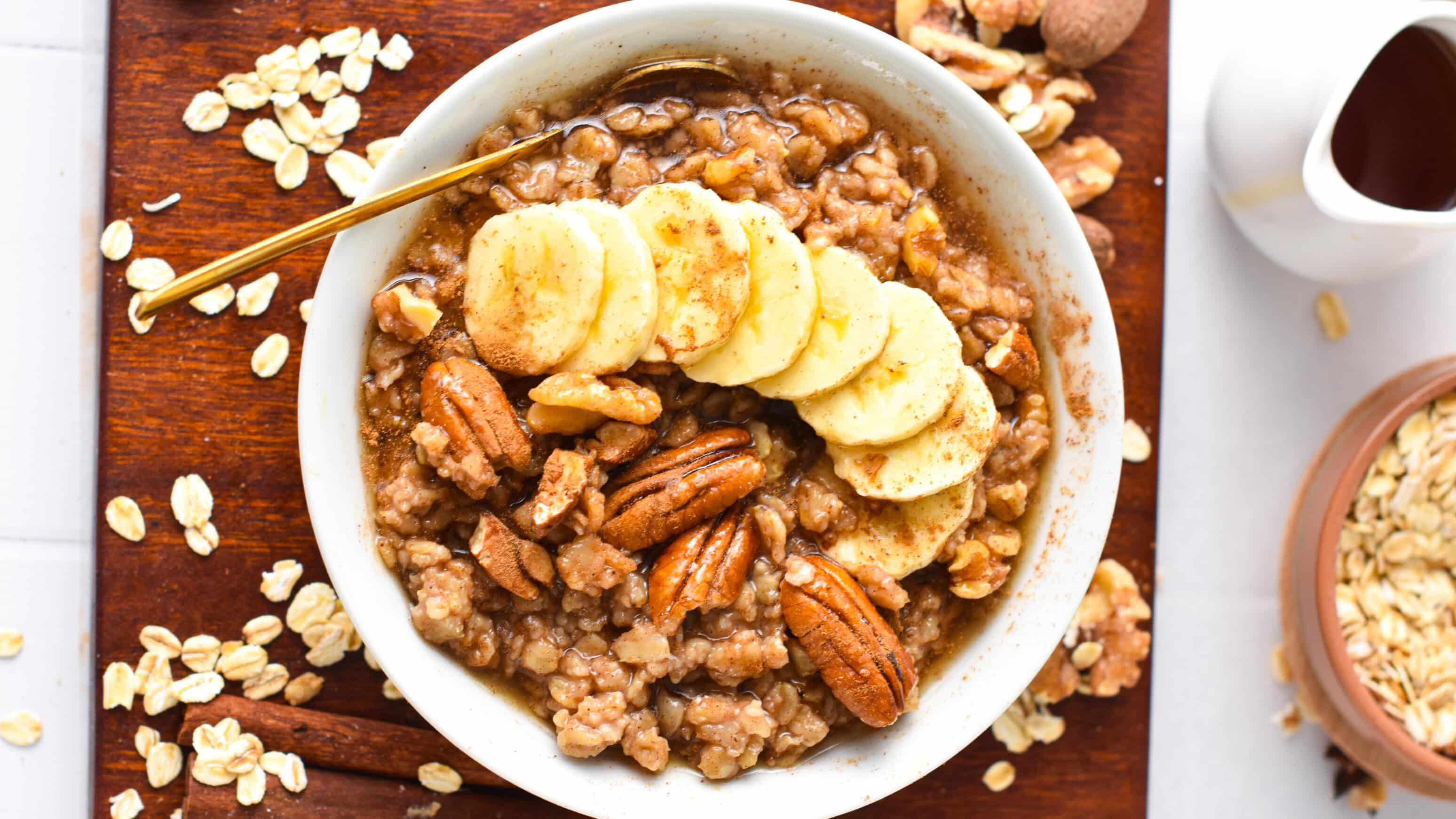 A bowl of cinnamon oatmeal from the top with banana slices, pecans and walnuts.