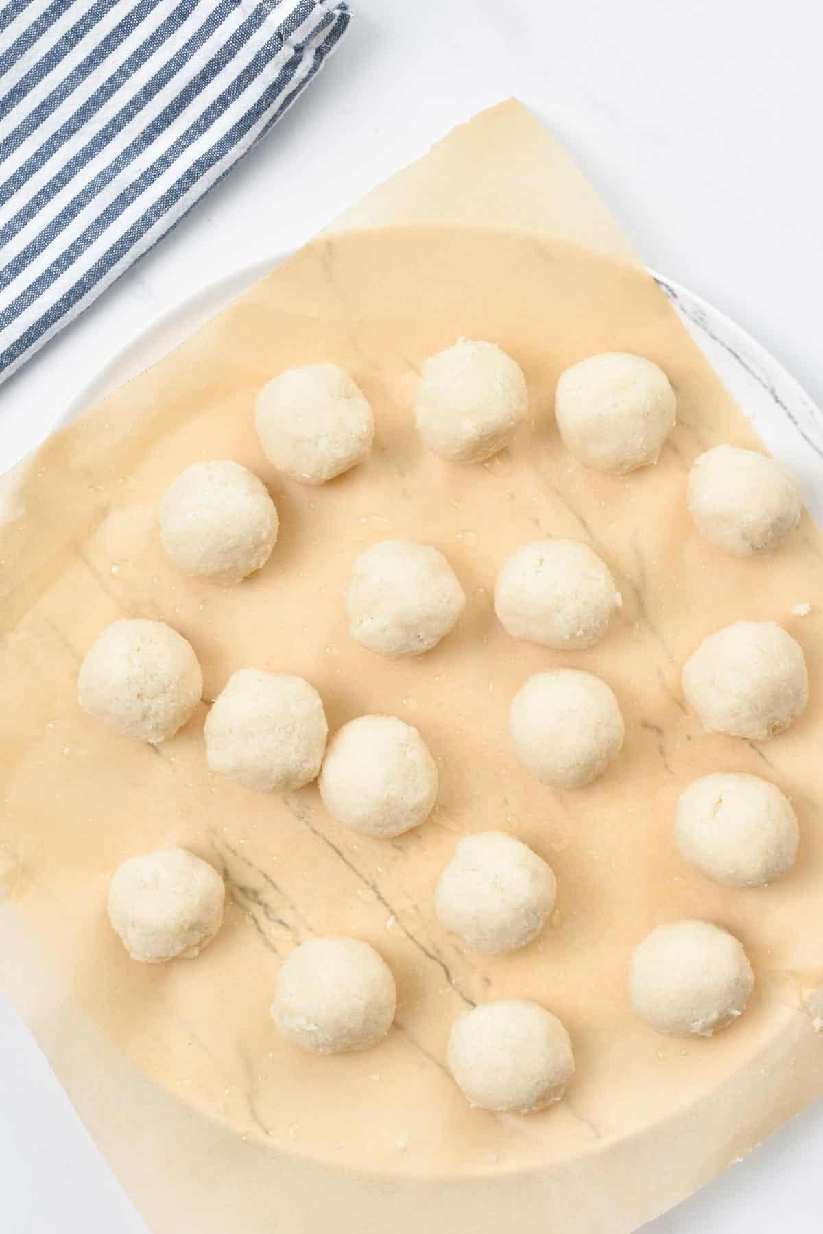 A plate with white coconut balls on parchment paper.