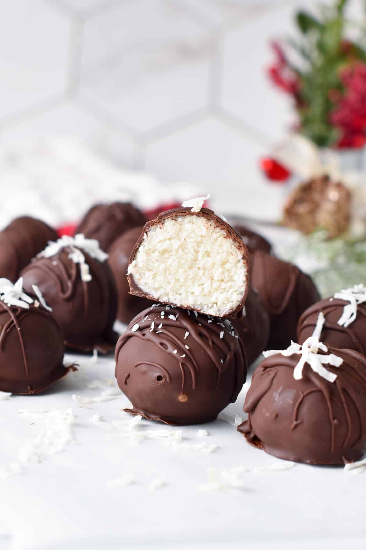 A stack of chocolate coconut balls with one balls cut halfway showing the coconut mixture inside