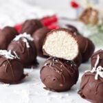 a stack of chocolate coconut balls with one balls cut halfway showing the coconut mixture inside