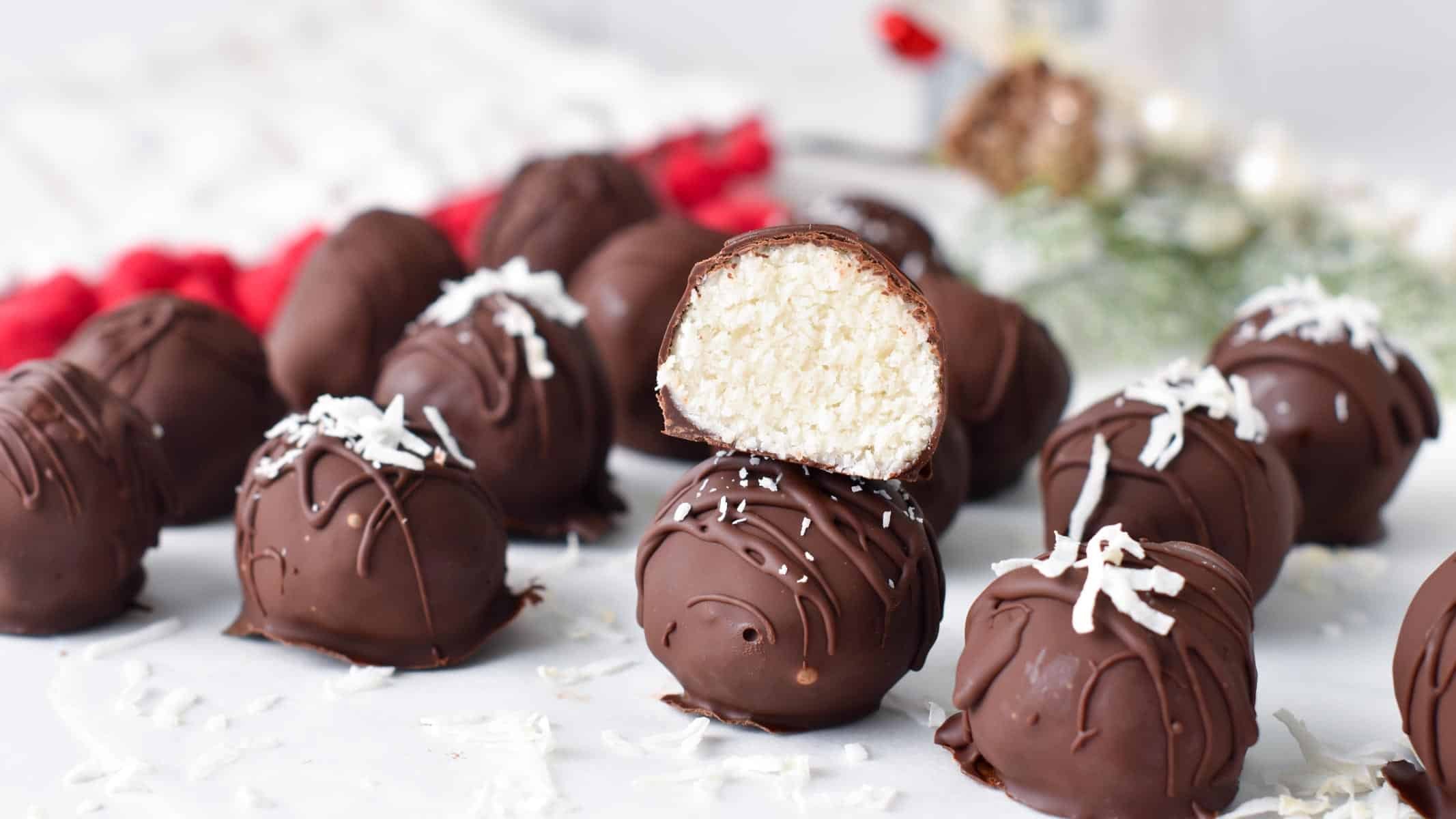 a stack of chocolate coconut balls with one balls cut halfway showing the coconut mixture inside