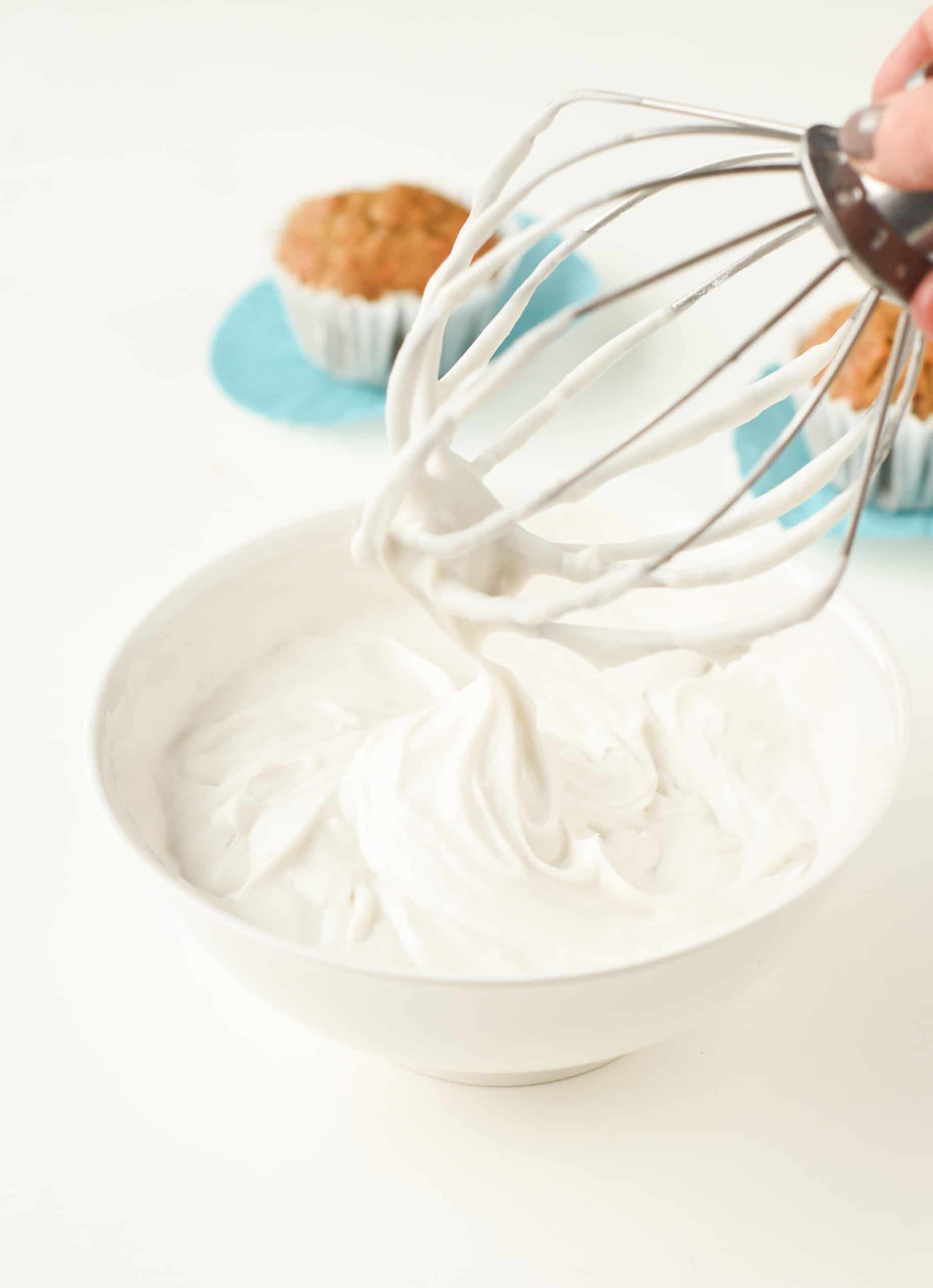Whipped coconut cream in a bowl with the whisk attachment of a stand mixer and a muffin in the background.