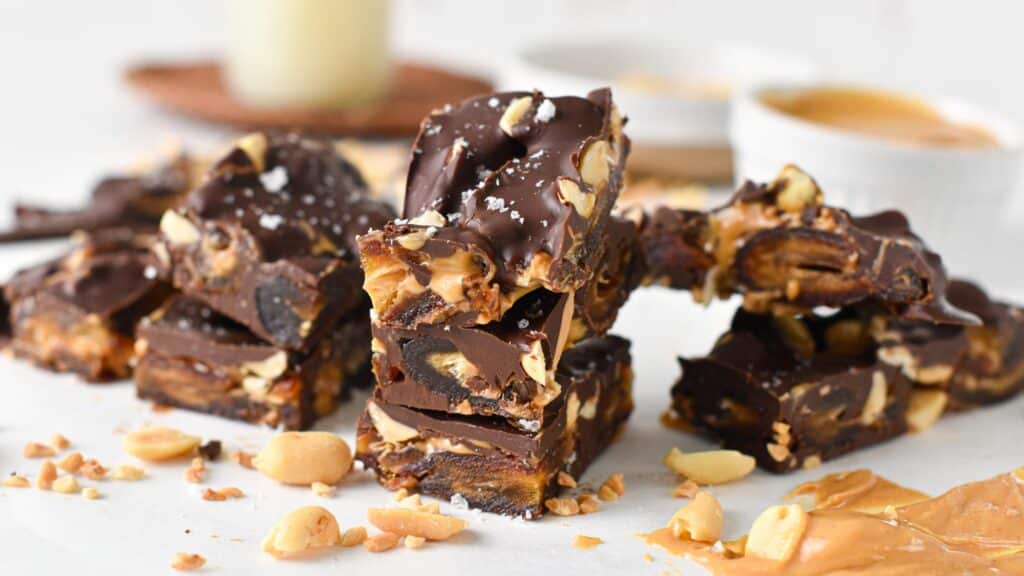 Pieces of date bark made with Medjool dates, peanuts, peanut butter and melted dark chocolate on a table.