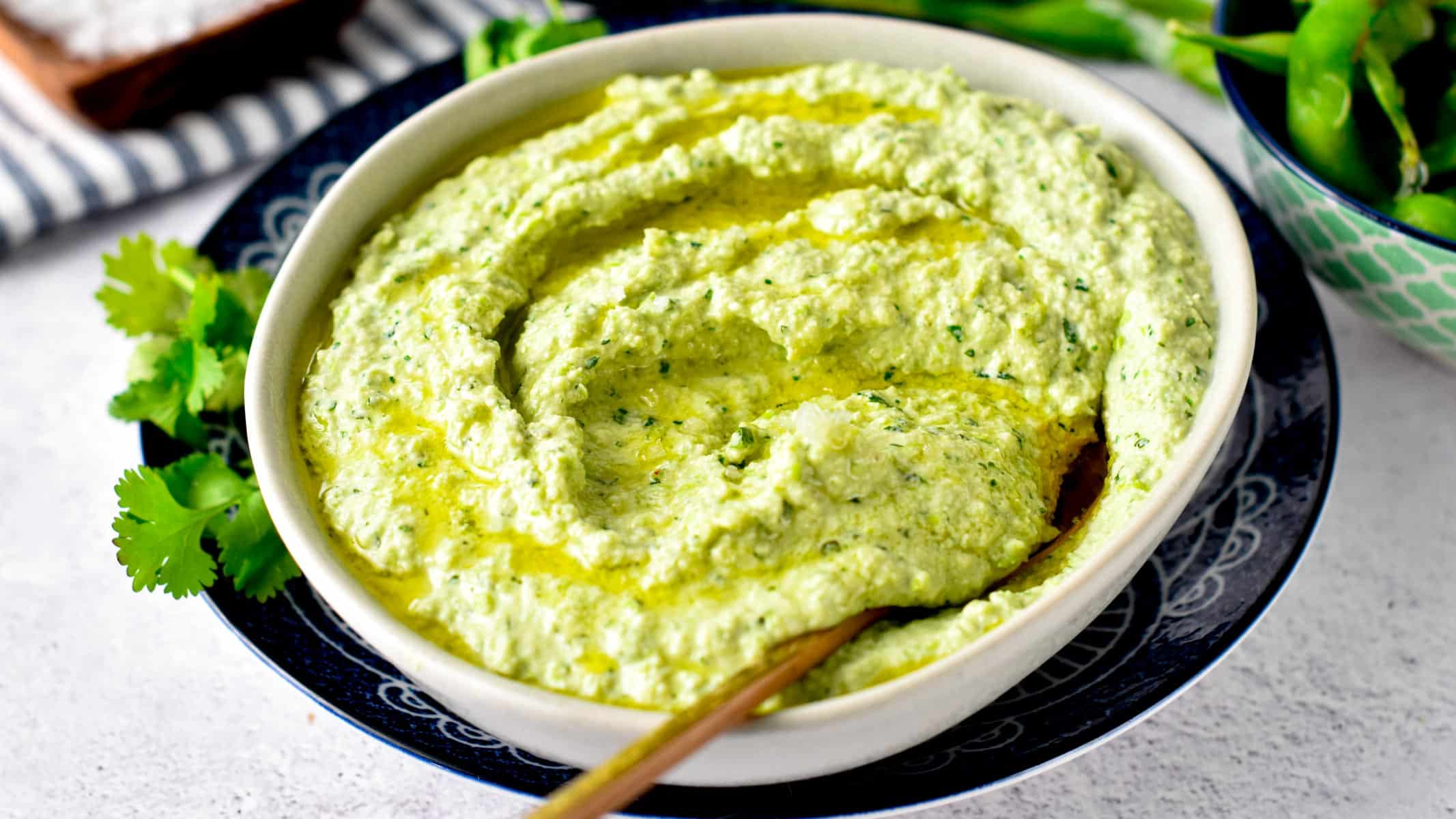 Edamame Hummus in a white bowl on a black plate with cilantro.