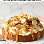 a single layer oat flour cake topped with dairy-free vanilal frosting, banana slices, walnuts, pecans, and peanut butter caramel