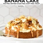 a oat flour banana cake topped with dairy-free vanilal frosting, banana slices, walnuts, pecans, and peanut butter caramel