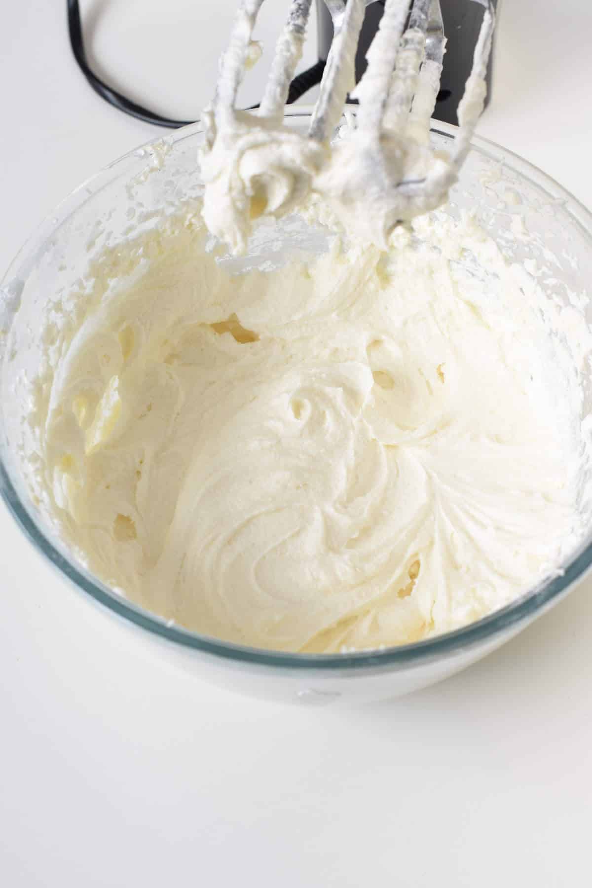 Vegan Vanilla Frosting in a mixing bowl with the blades of the whisker visible on top.