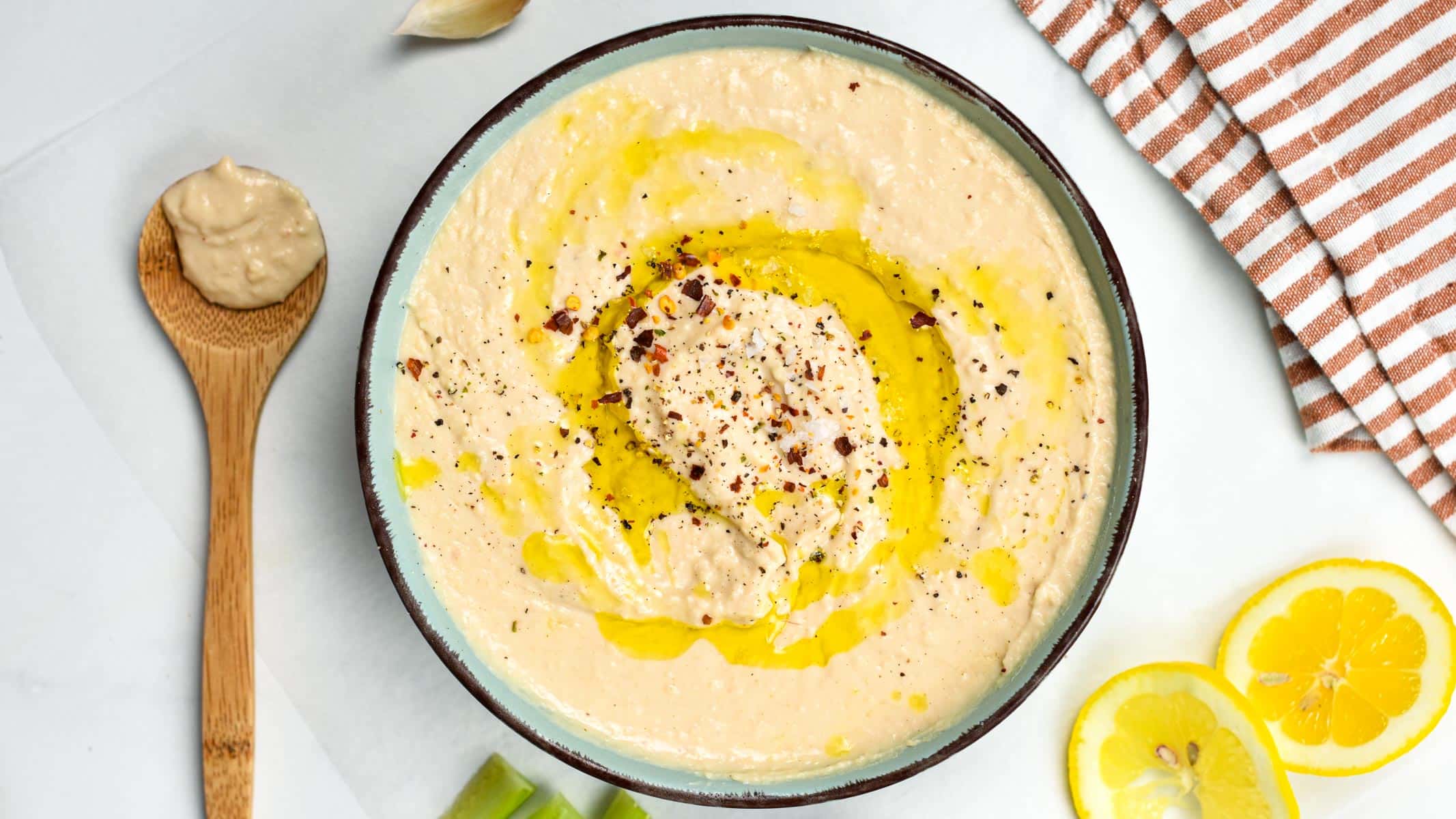 Vegan White Bean Dip next to a wooden spoon and lemon slices.