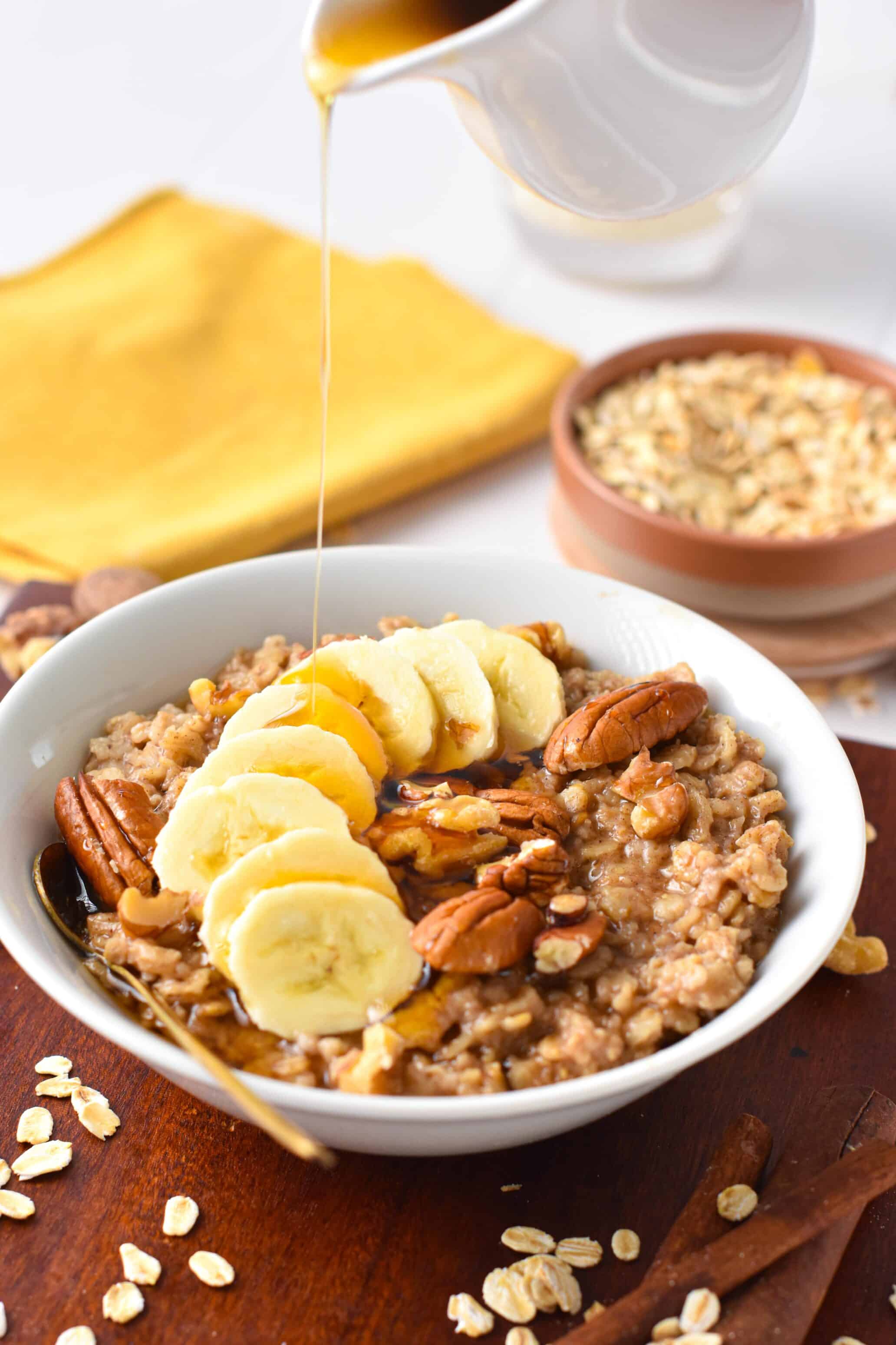 A bowl of vegan oatmeal with banana slices, pecans and walnuts.