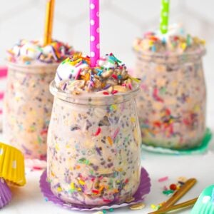glass mason jars filled with birthday cake overnight oats and a candle on top