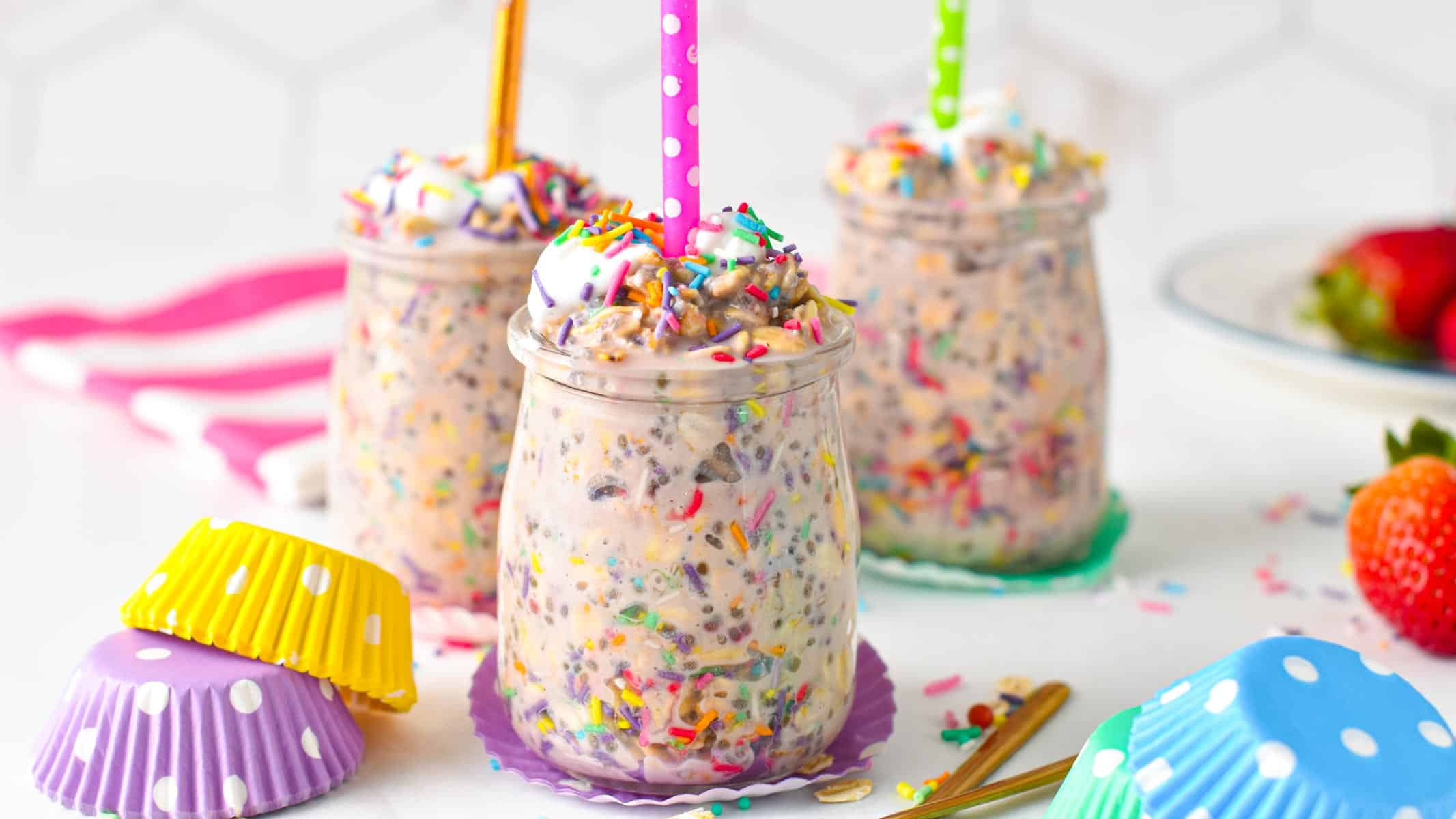 Three glass mason jars filled with birthday cake overnight oats and a candle on top of each.