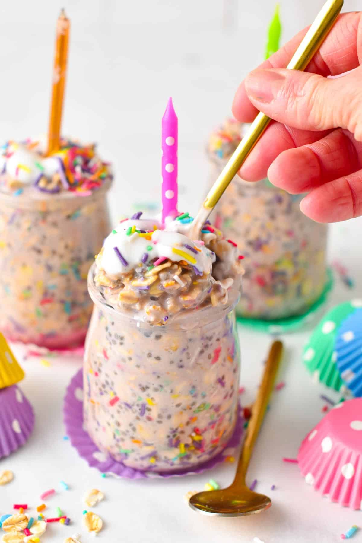 Glass mason jars filled with birthday cake overnight oats and a golden spoon digging in.