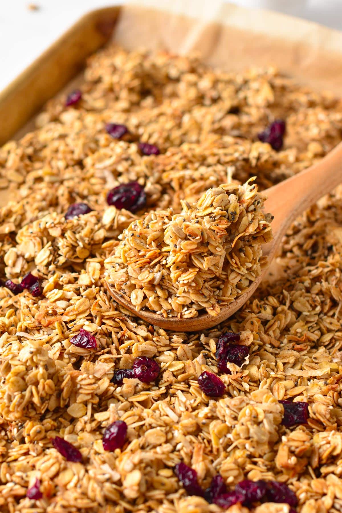 Nut-free granola cooling on a cooking sheet with a wooden spoon scooping a serving.