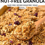 a large batch of nut-free granola on a baking sheet with a large wooden spoon filled with some of the granola recipe
