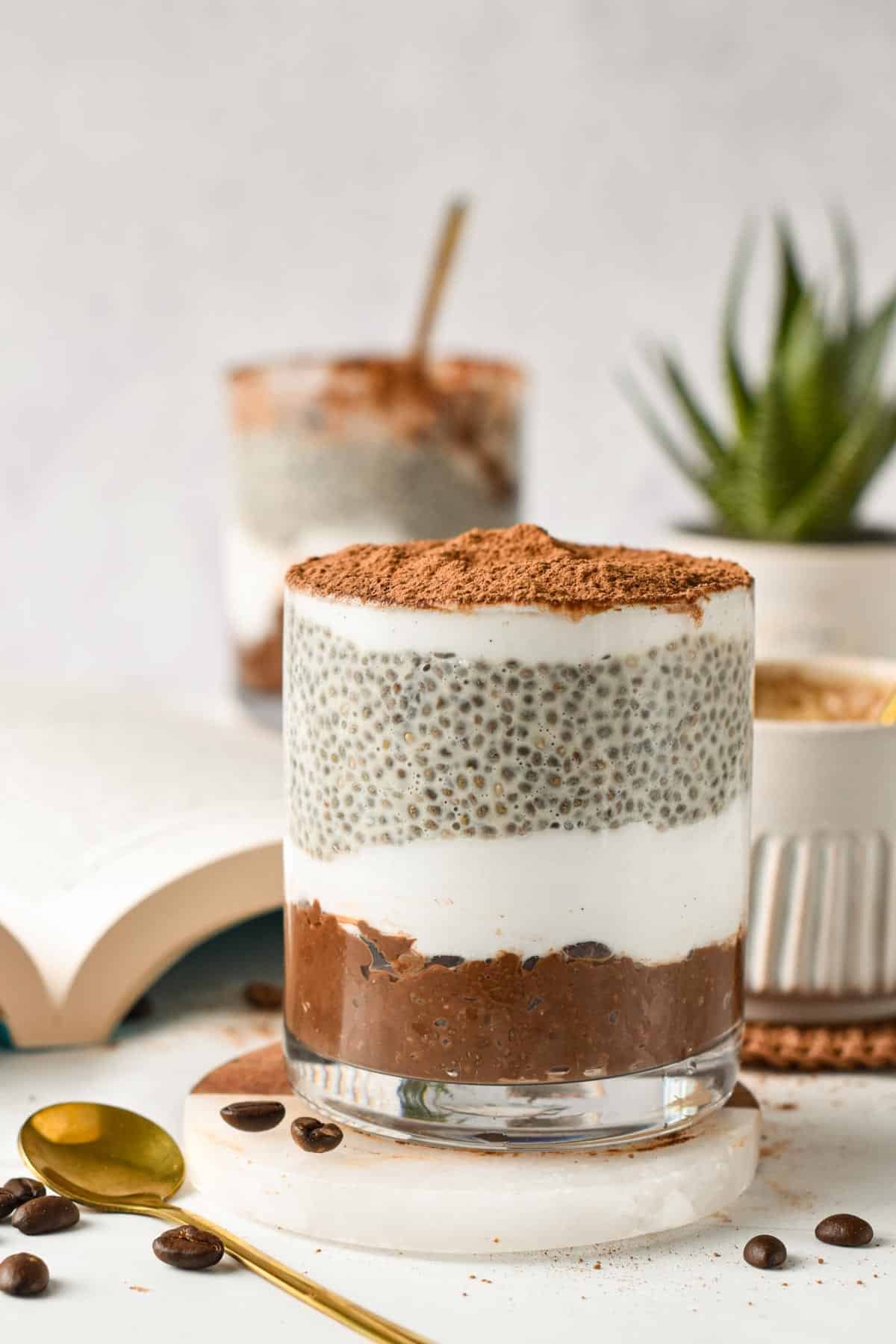 A glass jar filled with layers of vanilla chia pudding, yogurt, chocolate coffee chia pudding to form a tiramisu chia pudding.