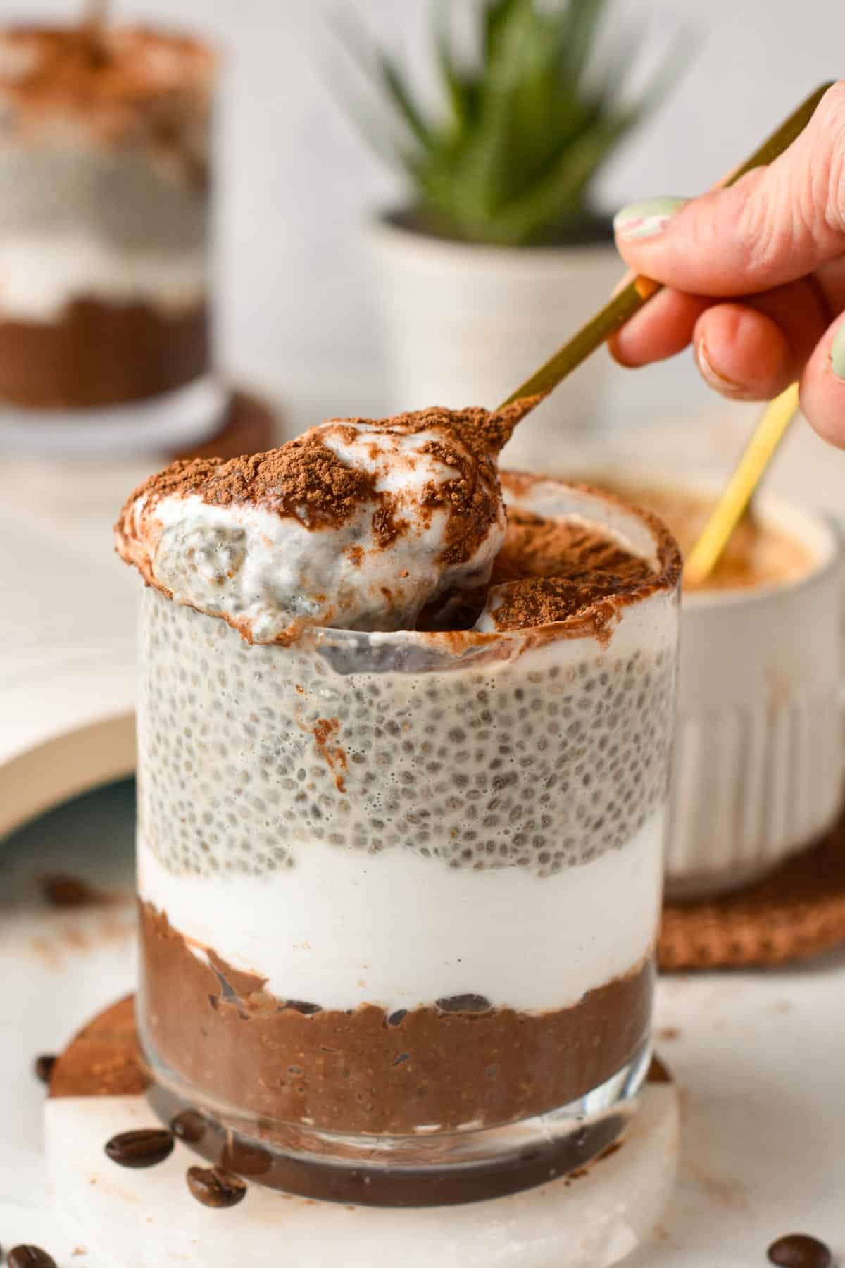 A spoon digging in a glass jar filled with tiramisu chia pudding.