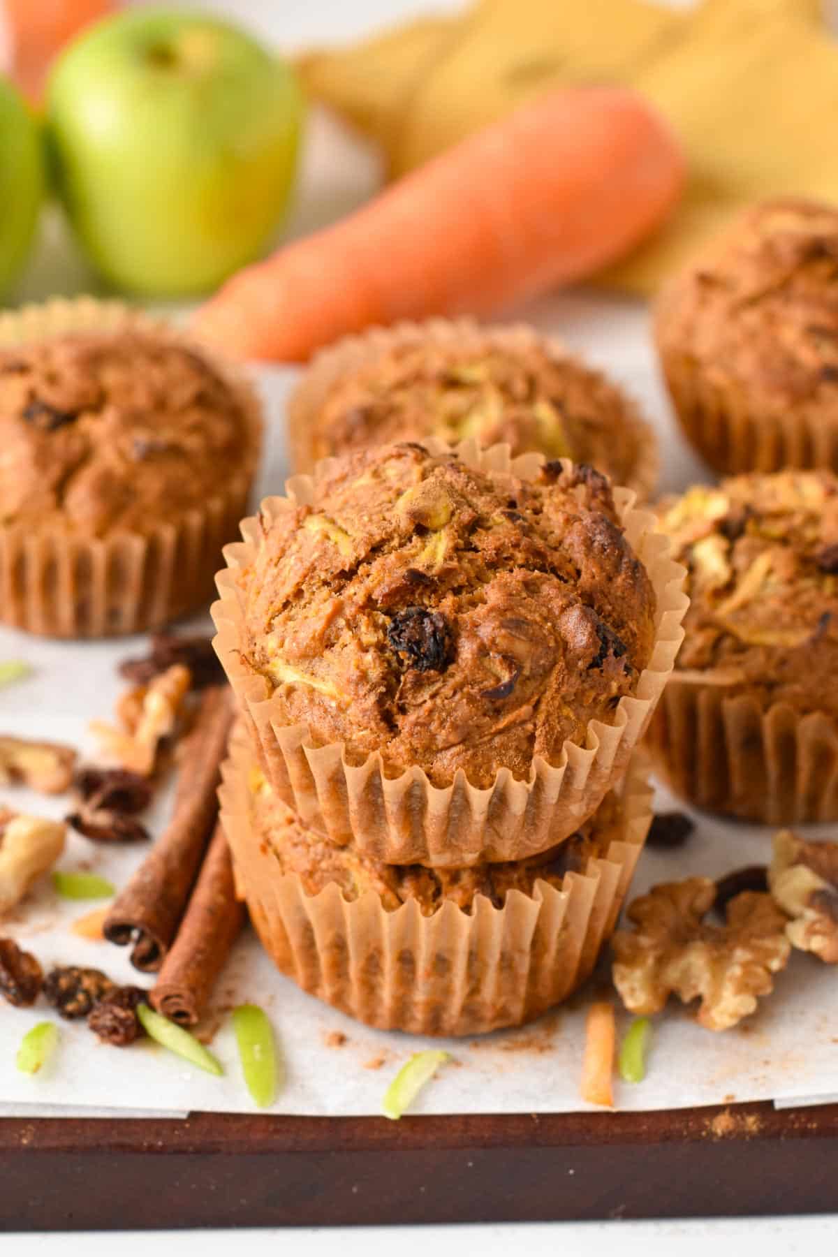 A batch of vegan Morning Glory Muffins with carrots and green apples in the background.