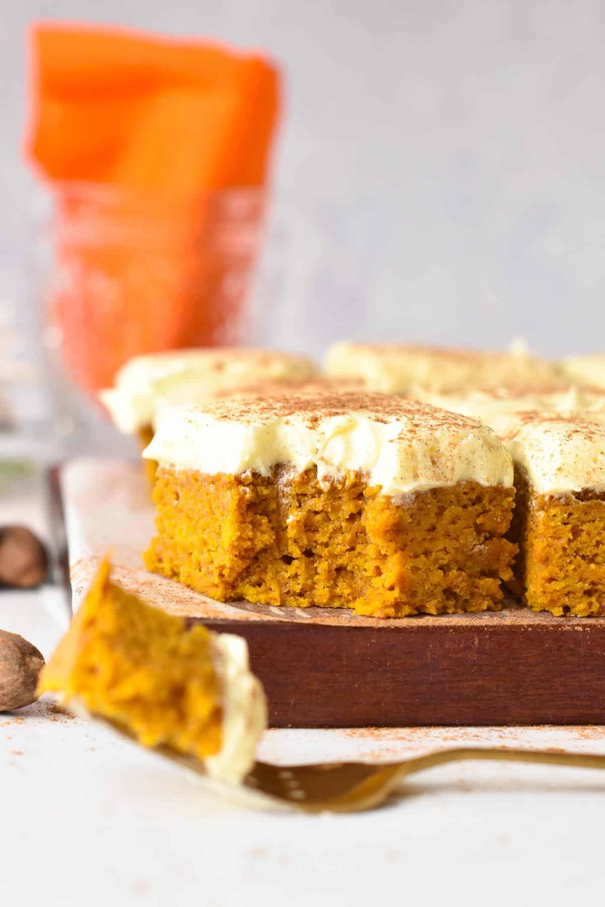 A slice of vegan pumpkin bars frosted with vanilla frosting on a wooden chopping board.