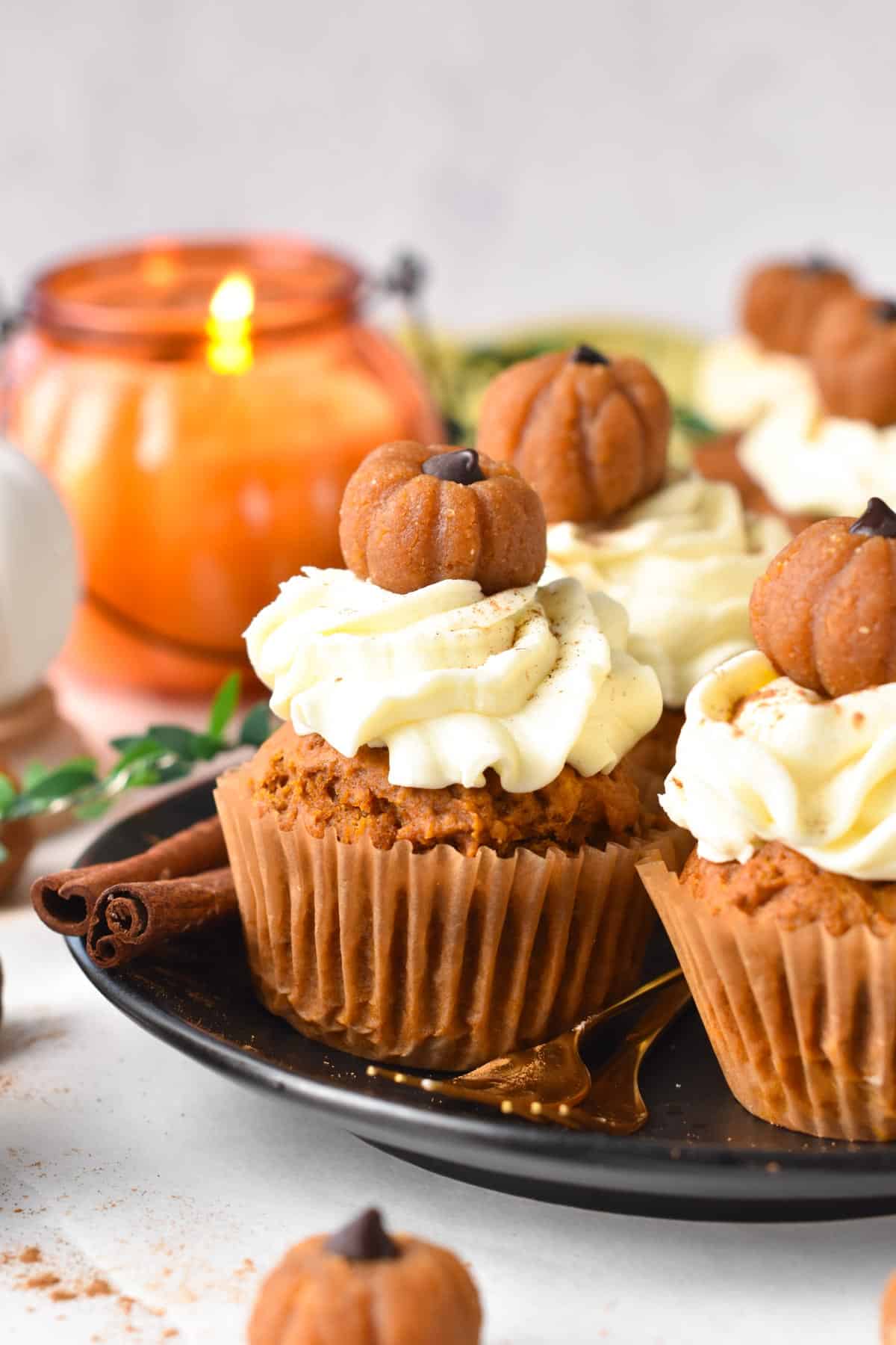 A plate filled with vegan pumpkin cupcakes frosted with vegan cream cheese frosting and little pumpkin cupcake topper