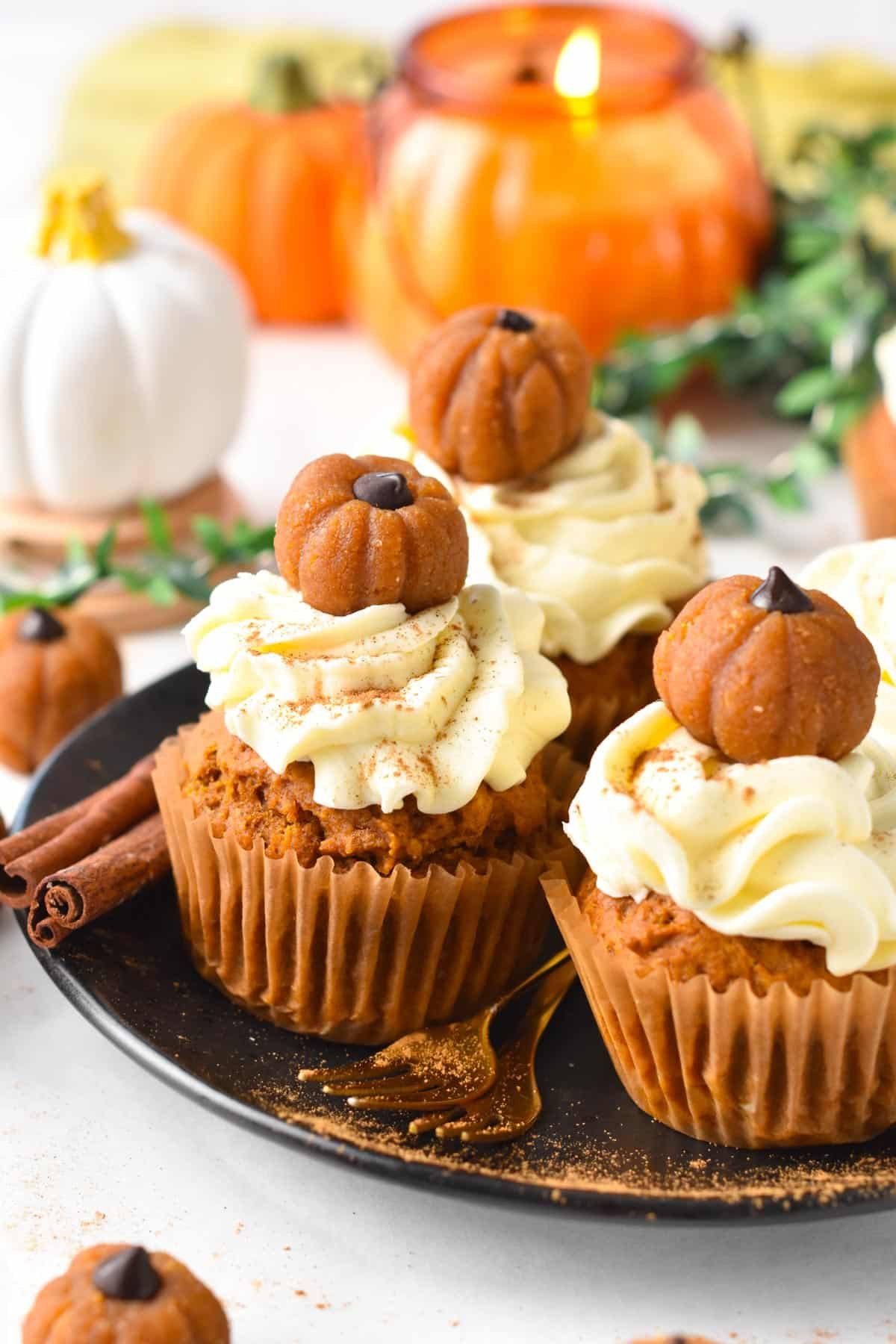 A plate filled with vegan pumpkin cupcakes frosted with vegan cream cheese frosting and little pumpkin cupcake topper.