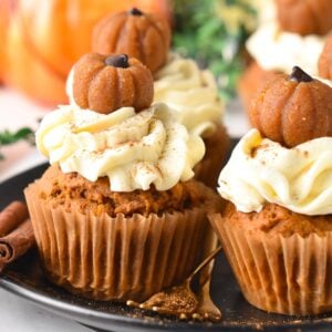 a plate filled with vegan pumpkin cupcakes frosted with vegan cream cheese frosting and little pumpkin cupcake topper