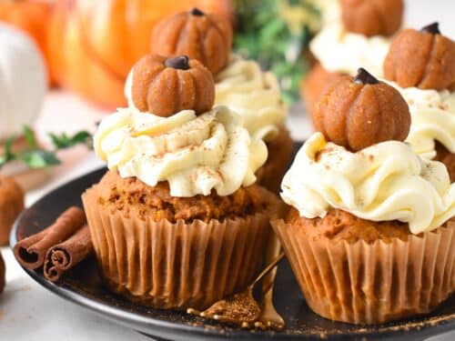 a plate filled with vegan pumpkin cupcakes frosted with vegan cream cheese frosting and little pumpkin cupcake topper