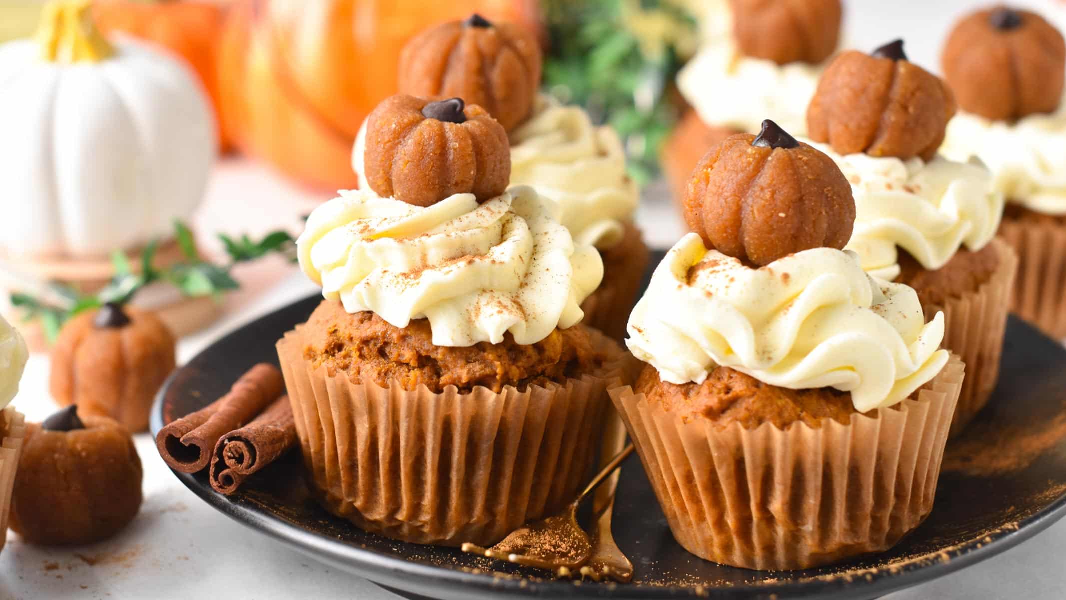 a plate filled with vegan pumpkin cupcakes frosted with vegan cream cheese frosting and little pumpkin cupcake topper