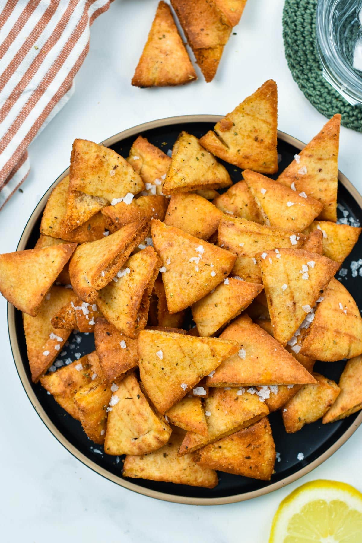 A black plate filled with baked pita chips and decorated with sea salt flakes.